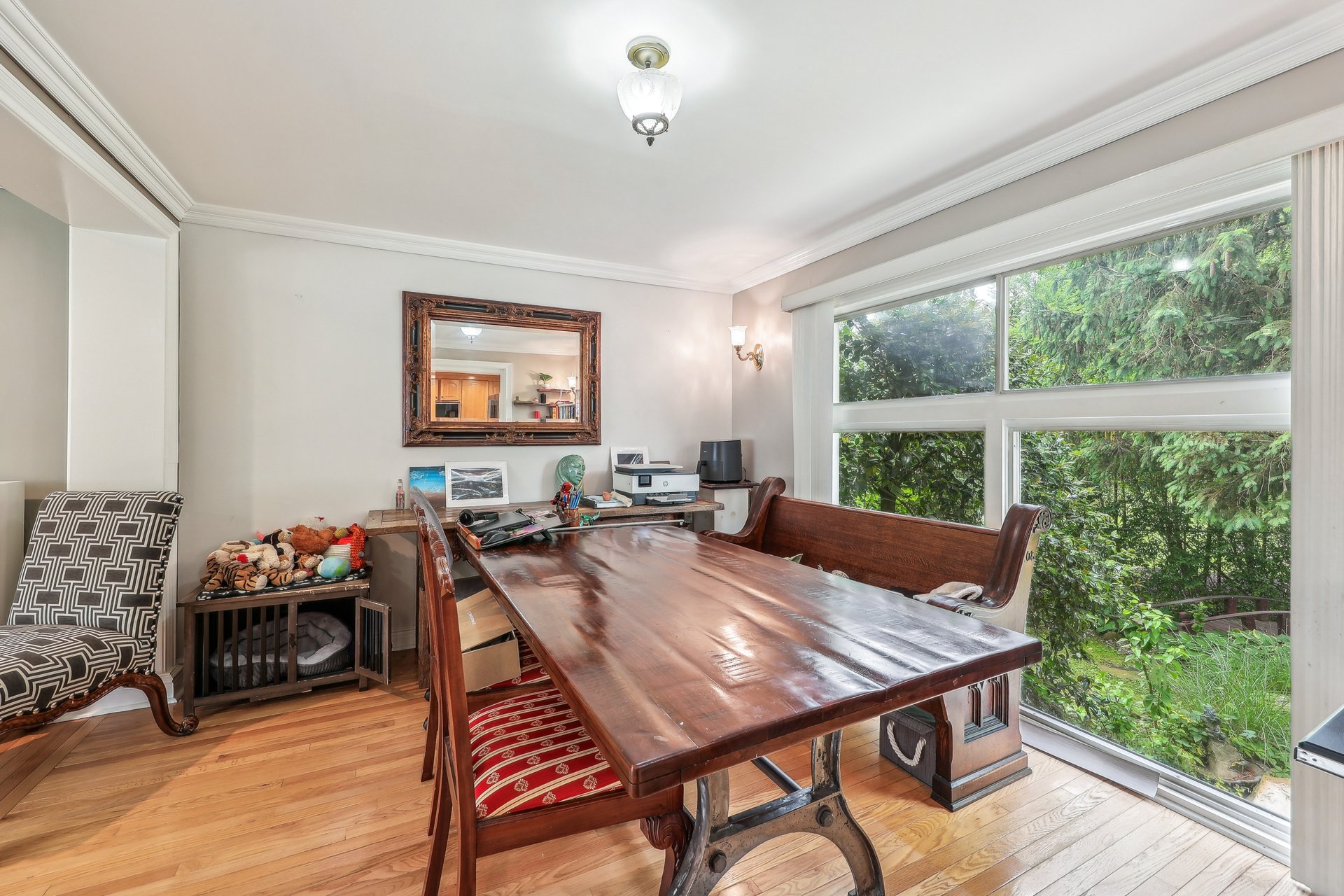 Dining room with a large polished wooden table and floor-to-ceiling windows overlooking greenery.