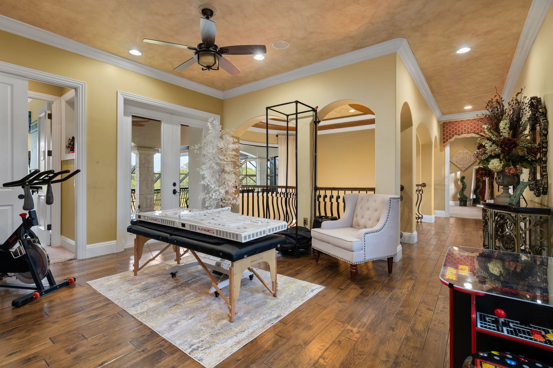 Home fitness room with a massage table, exercise bike, and arched hallway openings.