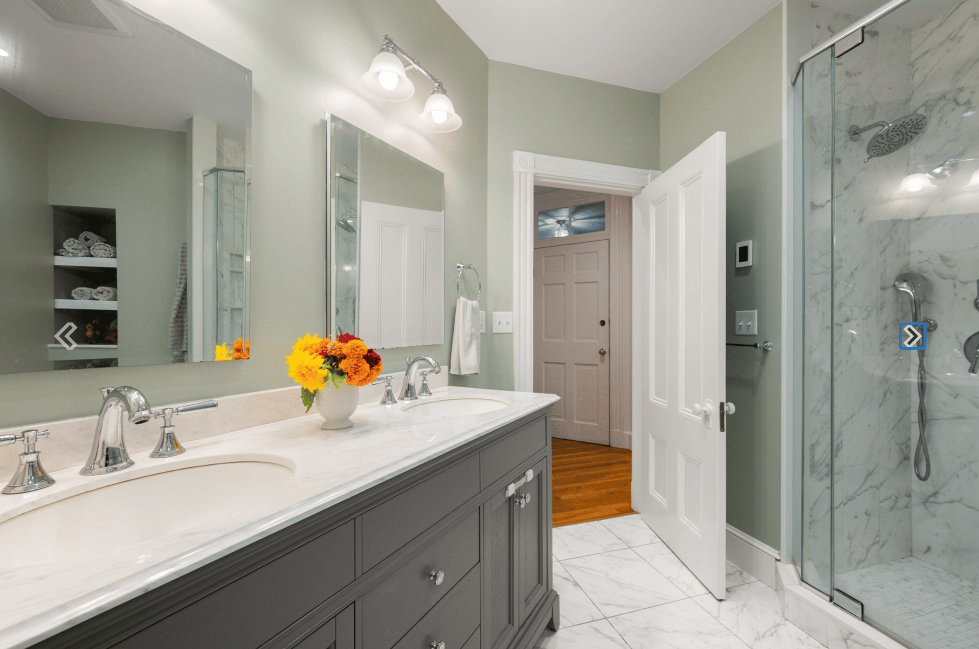 Bathroom with a gray double vanity, marble counters, and a glass-enclosed marble shower.