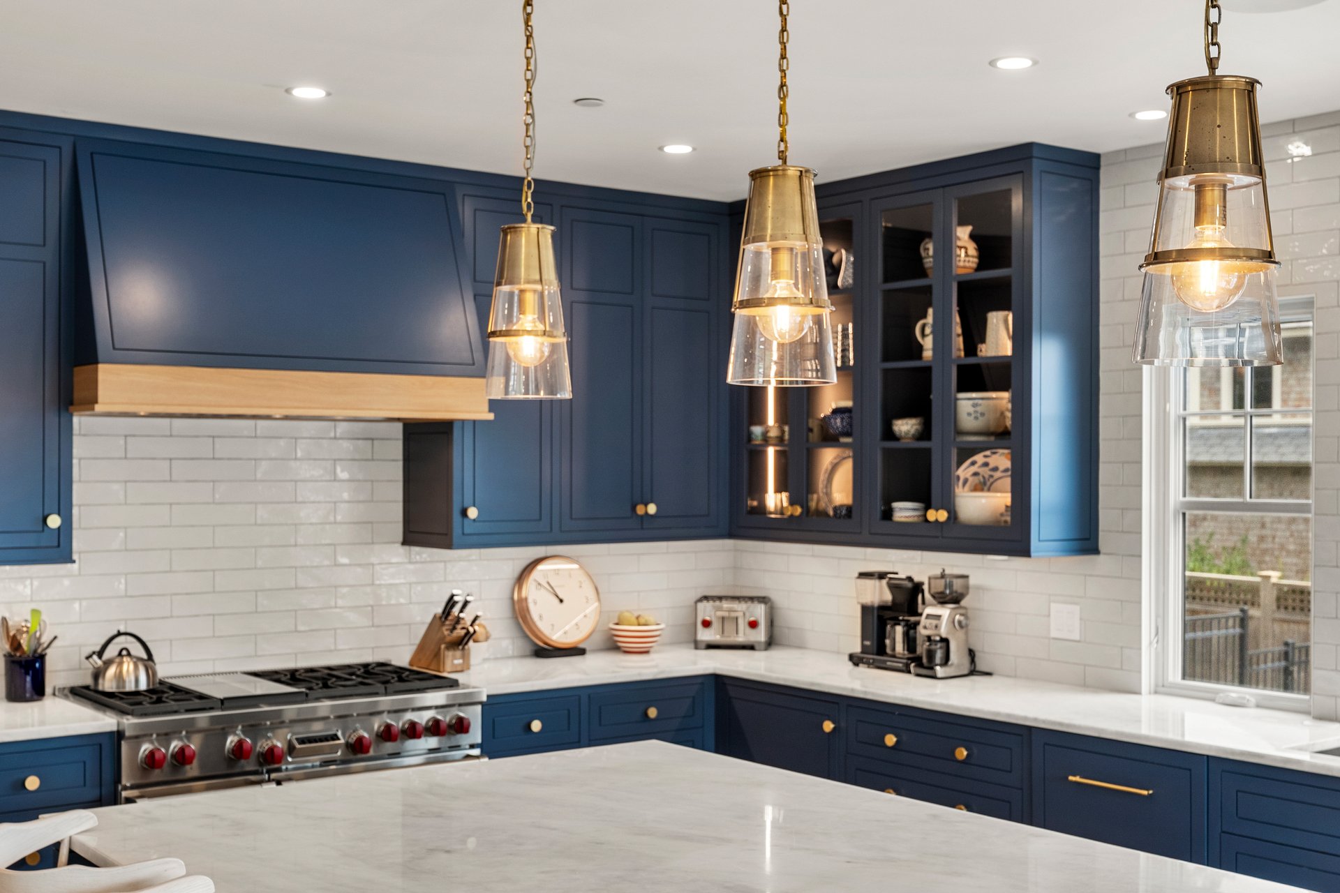 Kitchen with navy cabinetry, brass pendant lights, stainless steel range, and a large pale island.