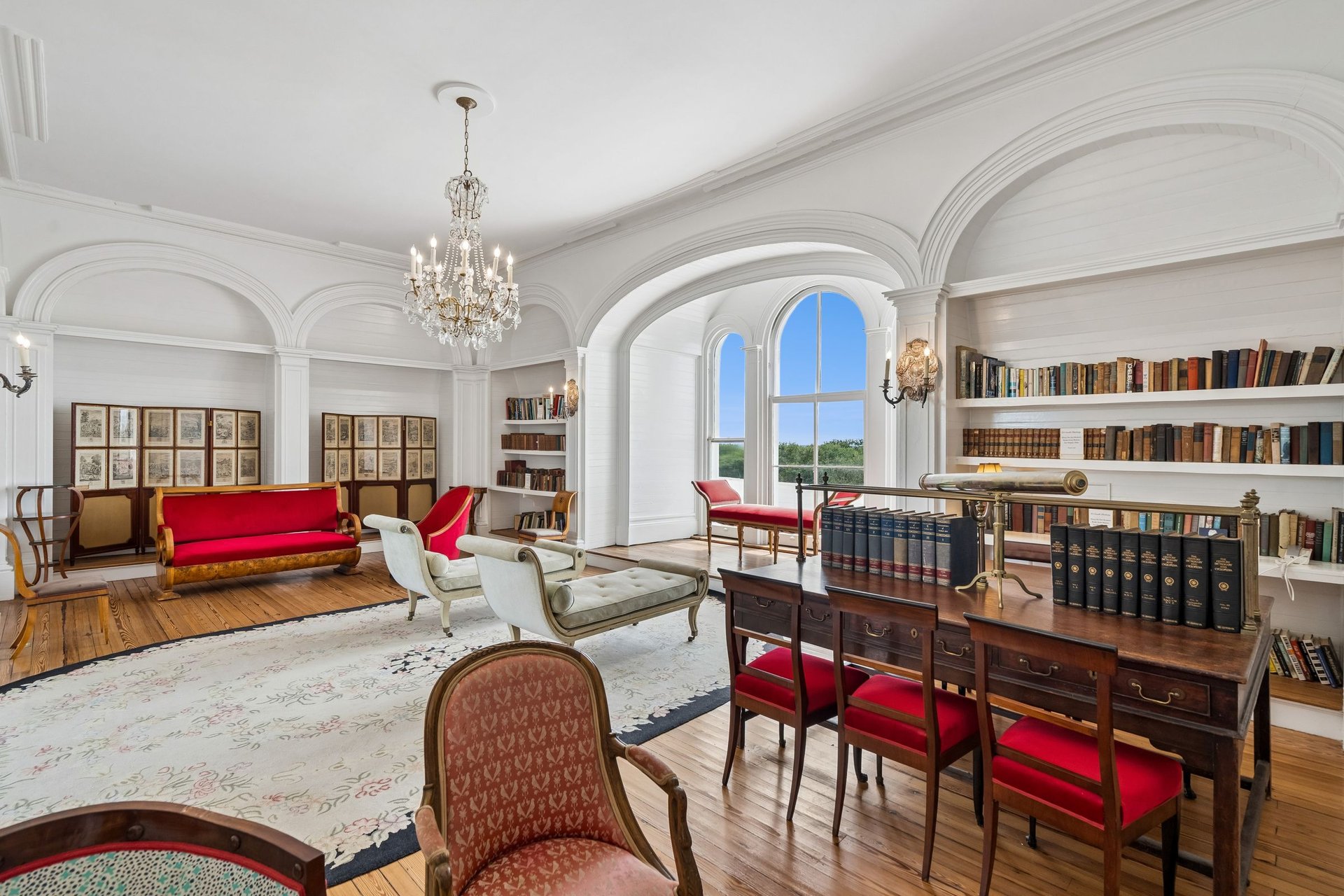 Historic library with arched ceilings, built-in bookshelves, a chandelier, and a large desk by tall windows.