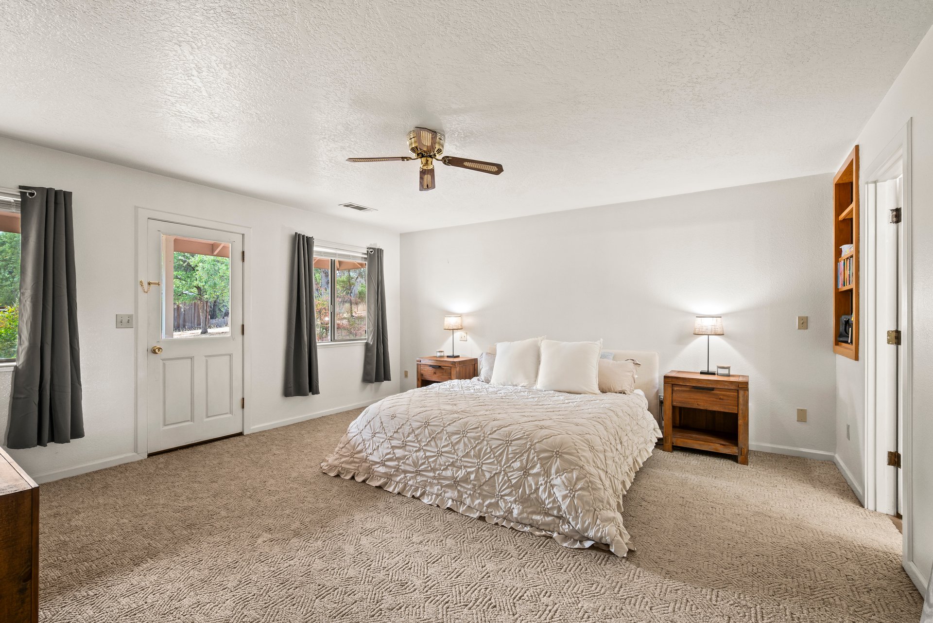 Bedroom with a large bed, beige carpet, and windows framed by dark curtains.