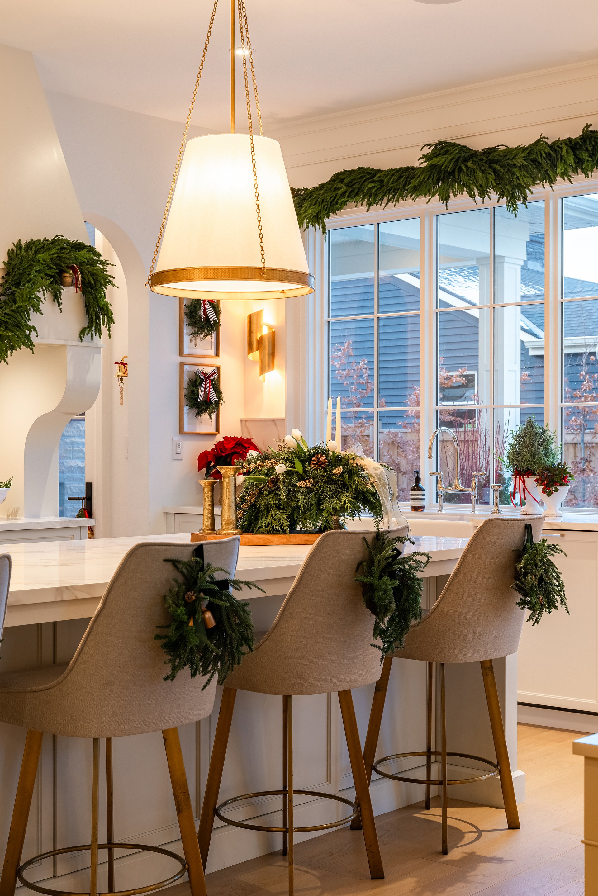 Holiday kitchen seating in an Oakville custom home with greenery on bar stools, marble island, brass lighting, and seasonal d&eacute;cor.