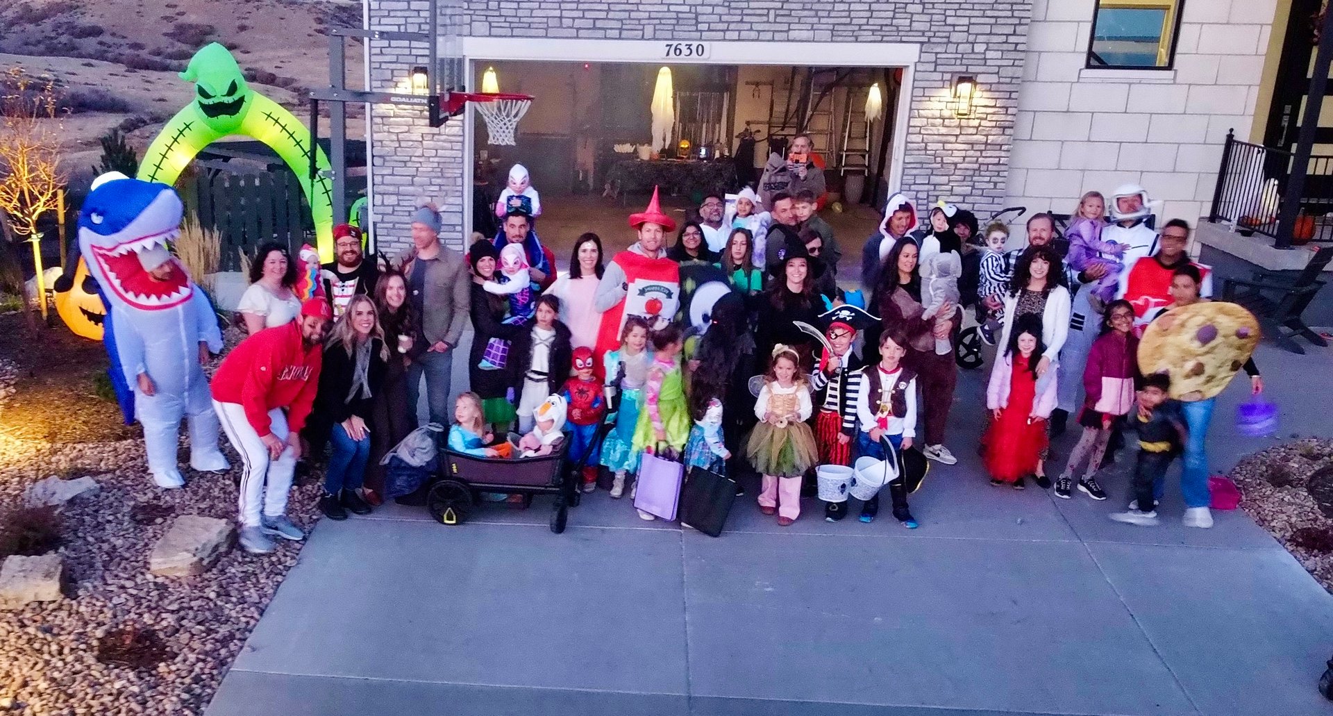 Neighbors in Halloween costumes gather for a group photo outside a decorated home.