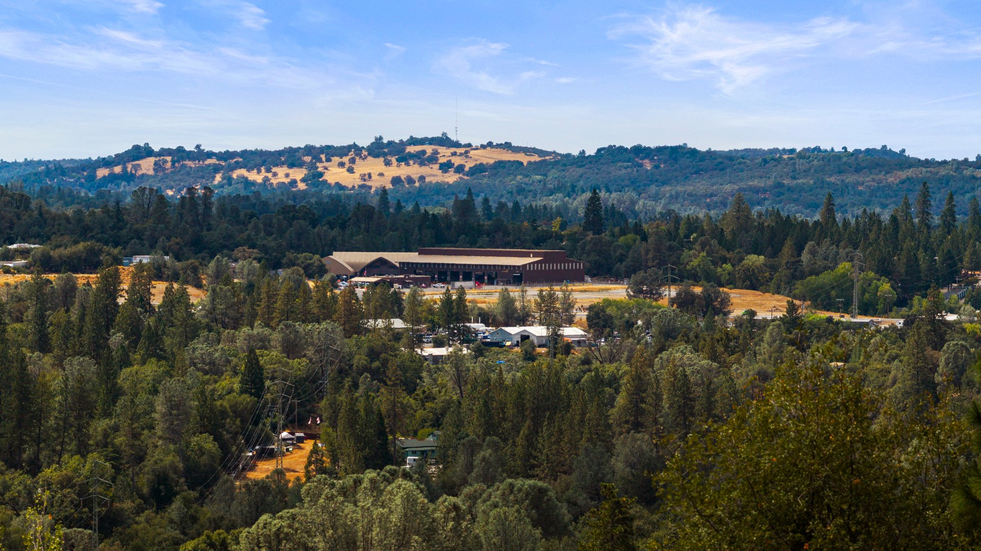 Panoramic view of wooded hills, scattered homes, and a large agricultural building in the valley.