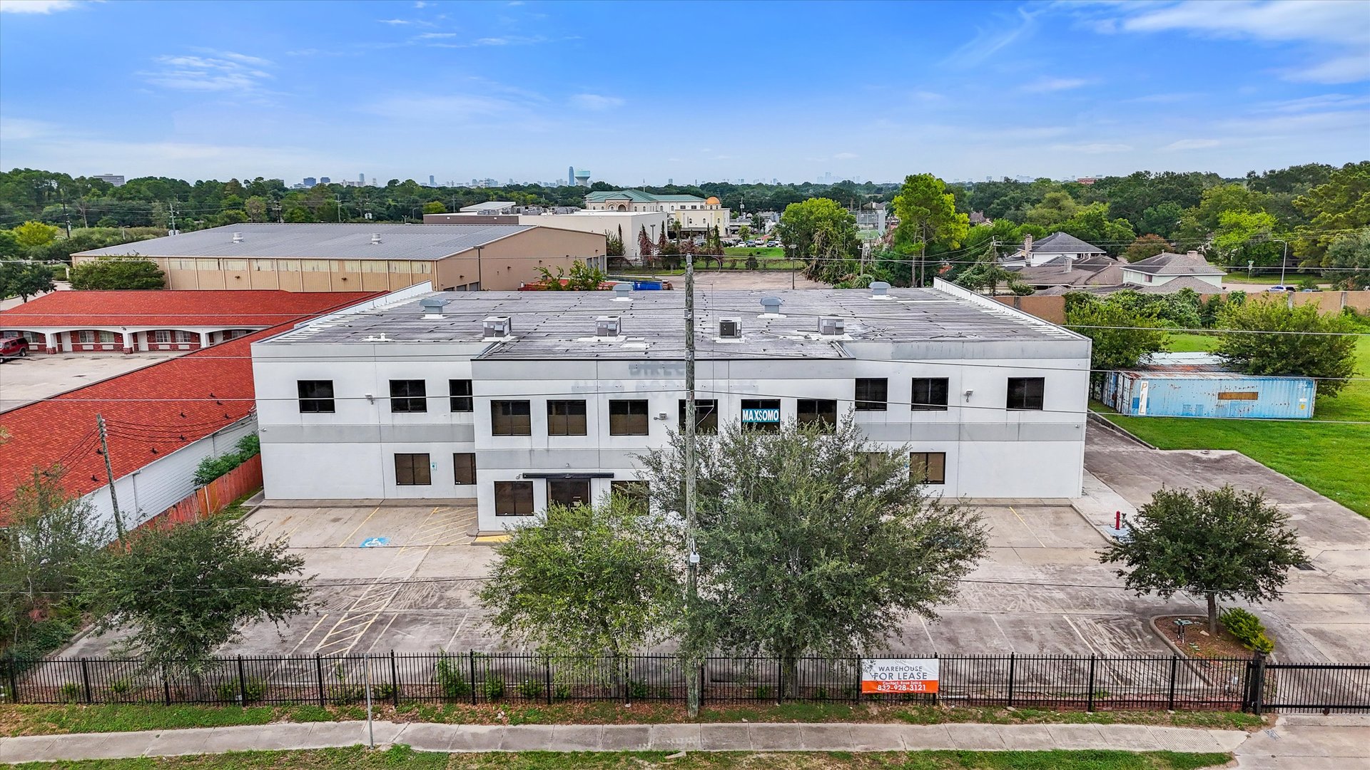 Aerial view of a white two-story warehouse with a flat roof and fenced parking area.