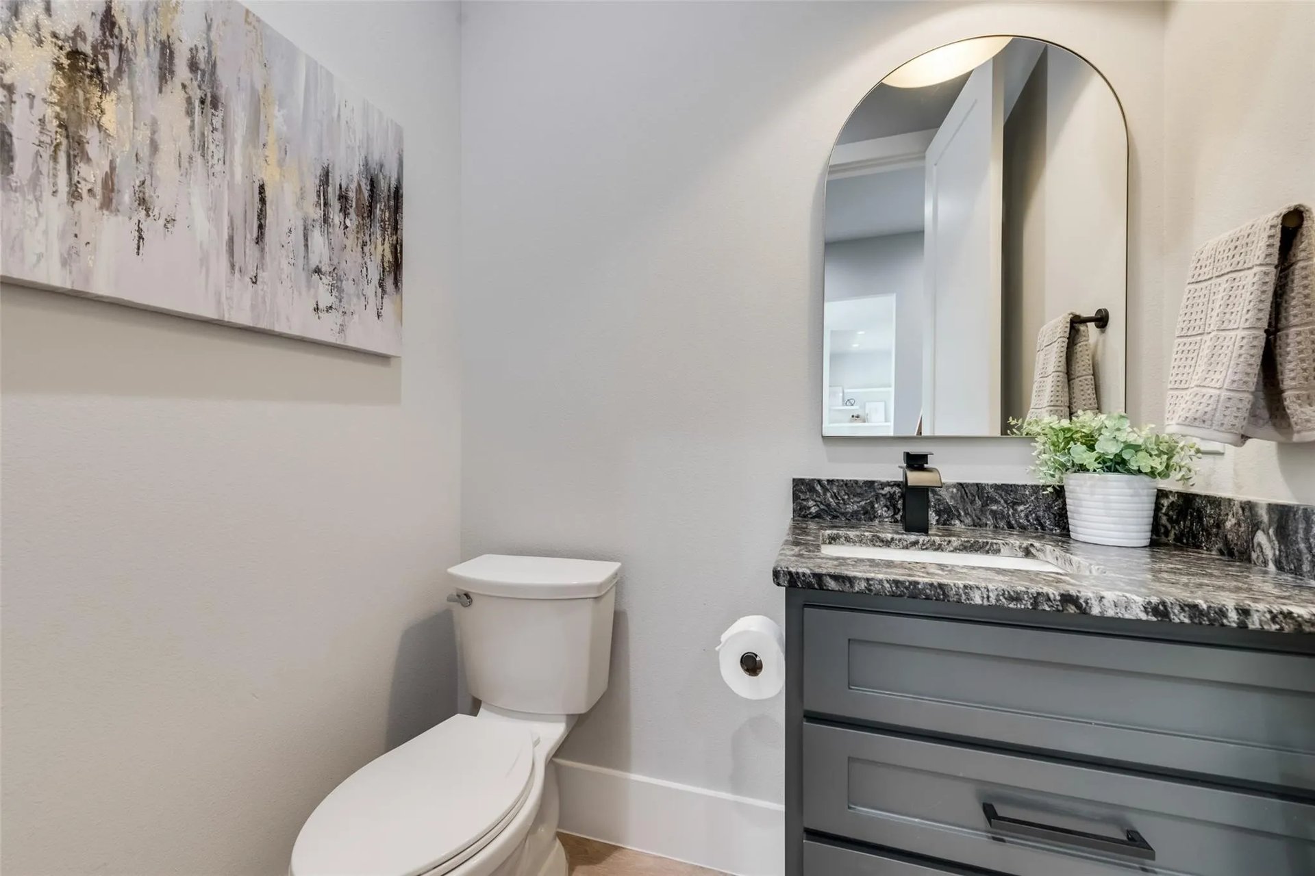 Bathroom with gray vanity, dark marbled countertop, arched mirror, and white toilet.