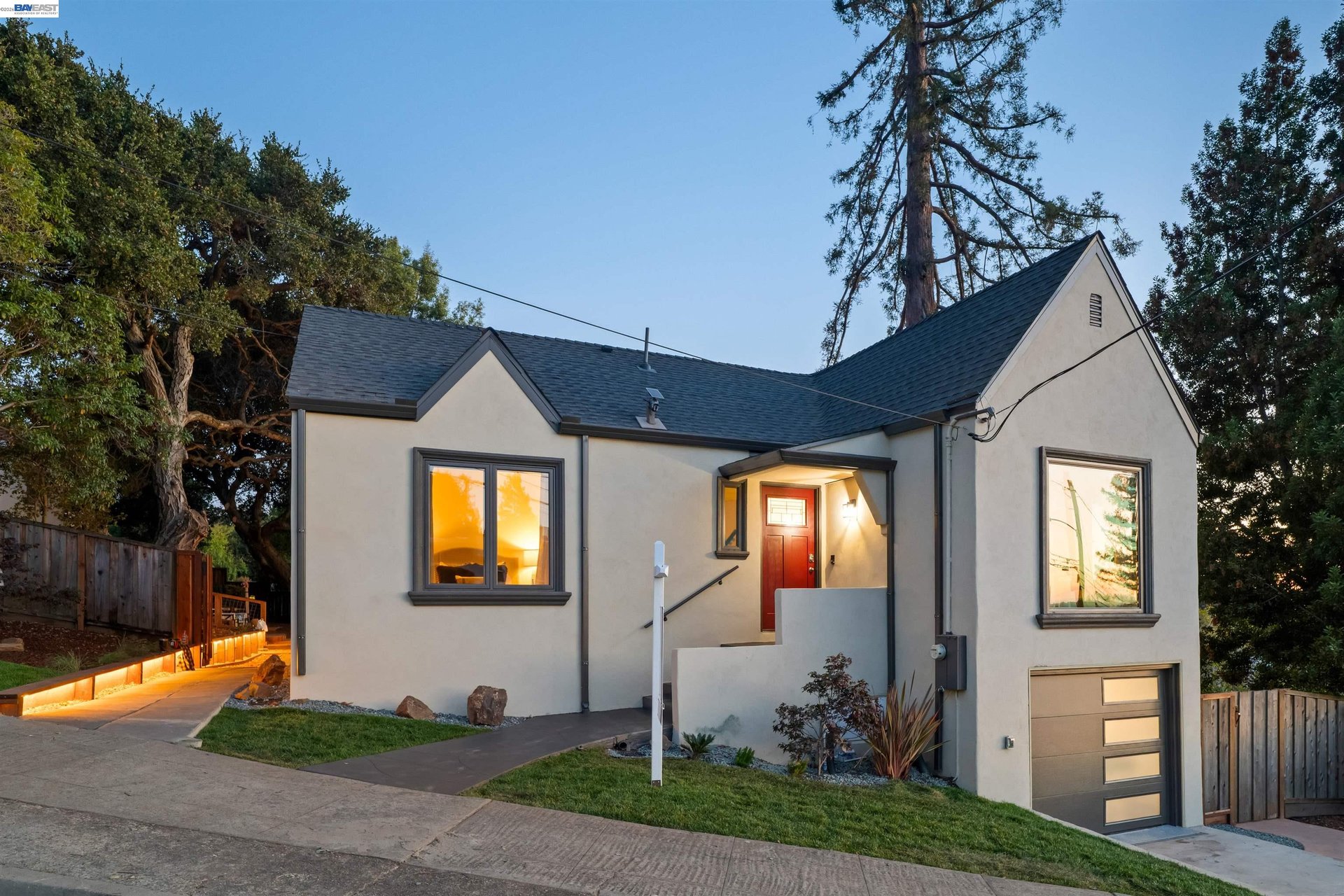 Home exterior at dusk with a red front door, attached garage, and illuminated entry path.