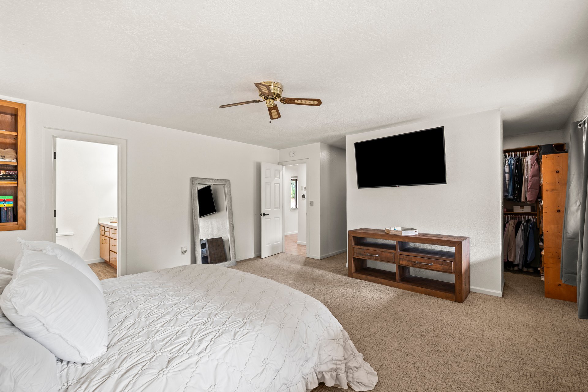 Bedroom with a white bed, wall-mounted television, ceiling fan, and open walk-in closet.