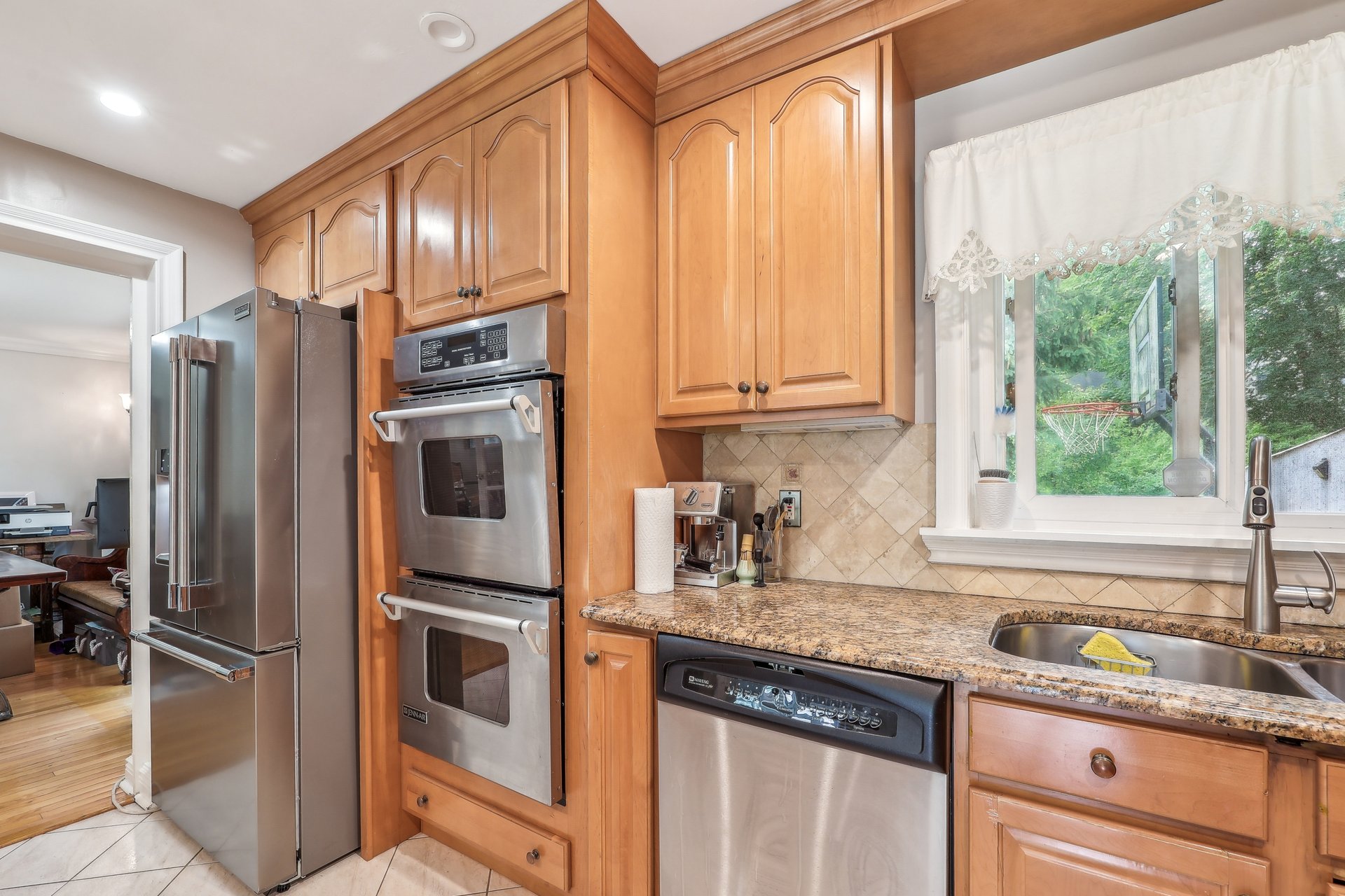 Kitchen with warm wood cabinets, stainless steel appliances, granite counters, and a window overlooking greenery.