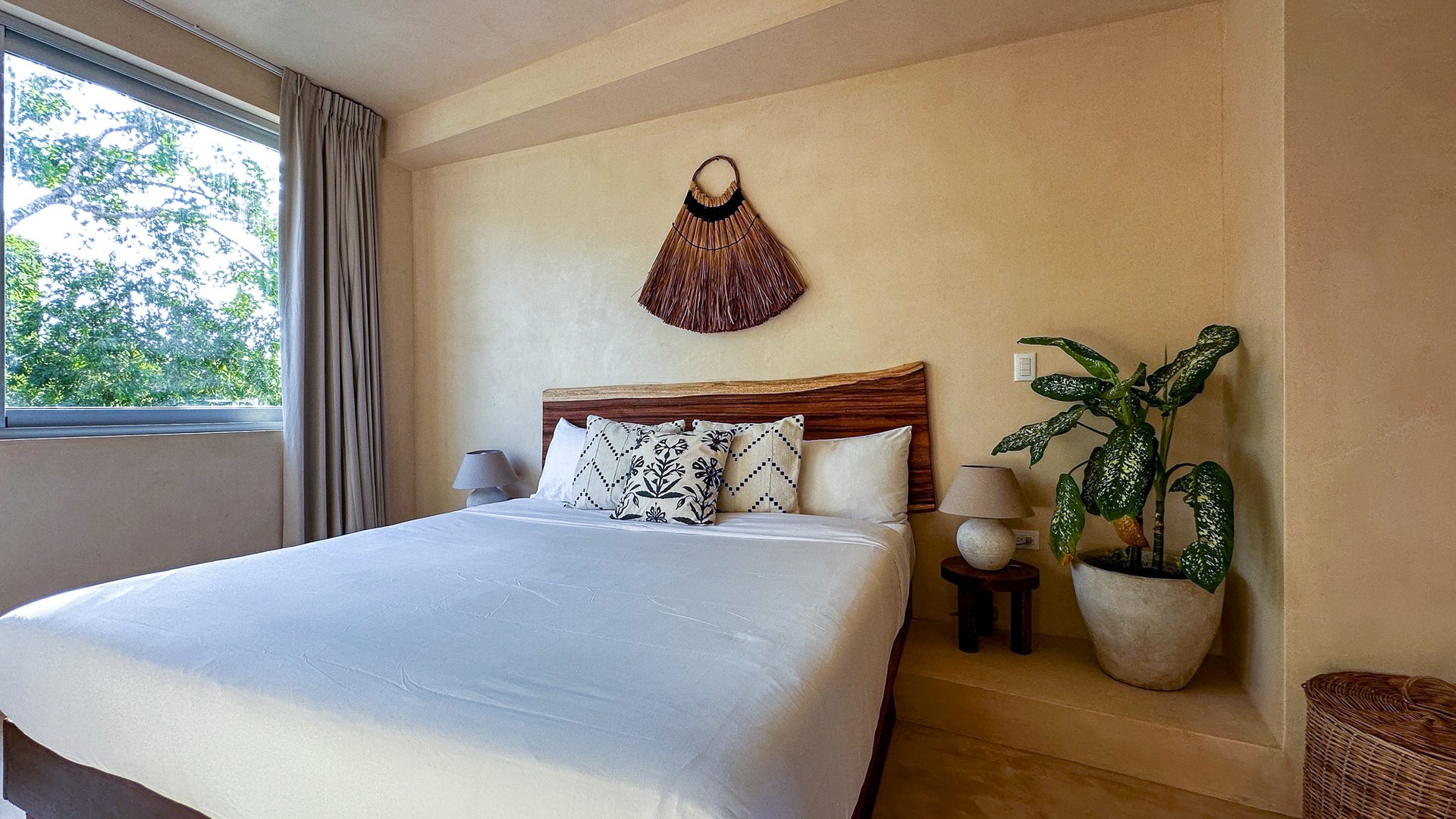 Bedroom with a king bed, carved wood headboard, patterned pillows, and a window overlooking trees.