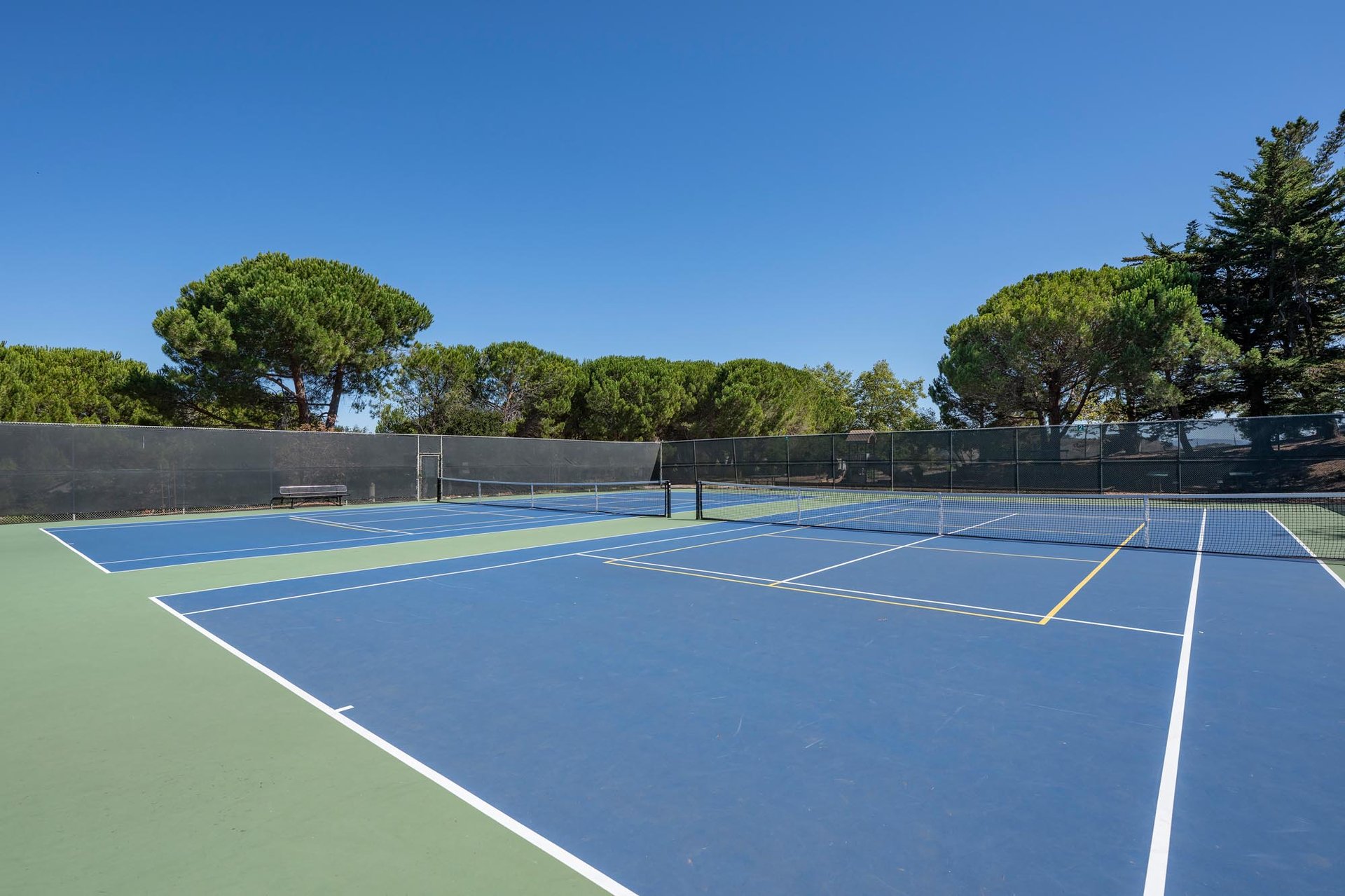 Clean and empty public tennis courts with blue and green surfaces, available for community use in Belmont, California.