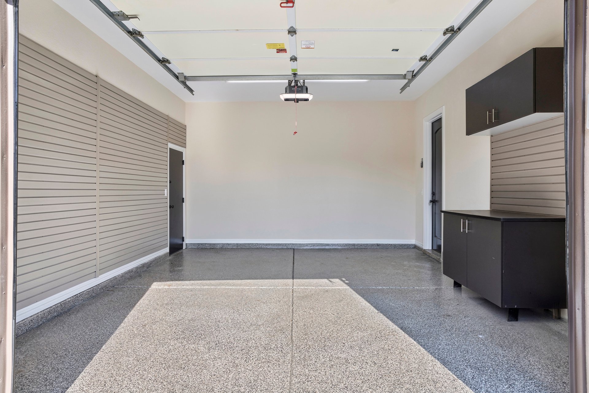 Finished garage interior with epoxy floor, slatwall panels, and storage cabinets.