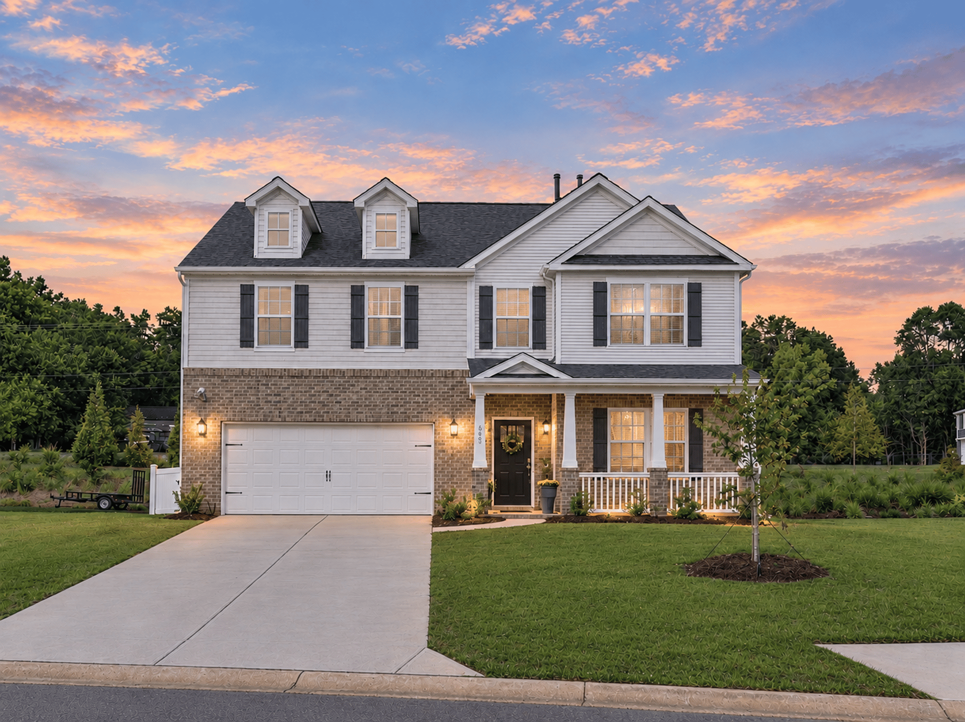 Two-story white and brick house with dormers, a front porch, and attached garage at sunset.