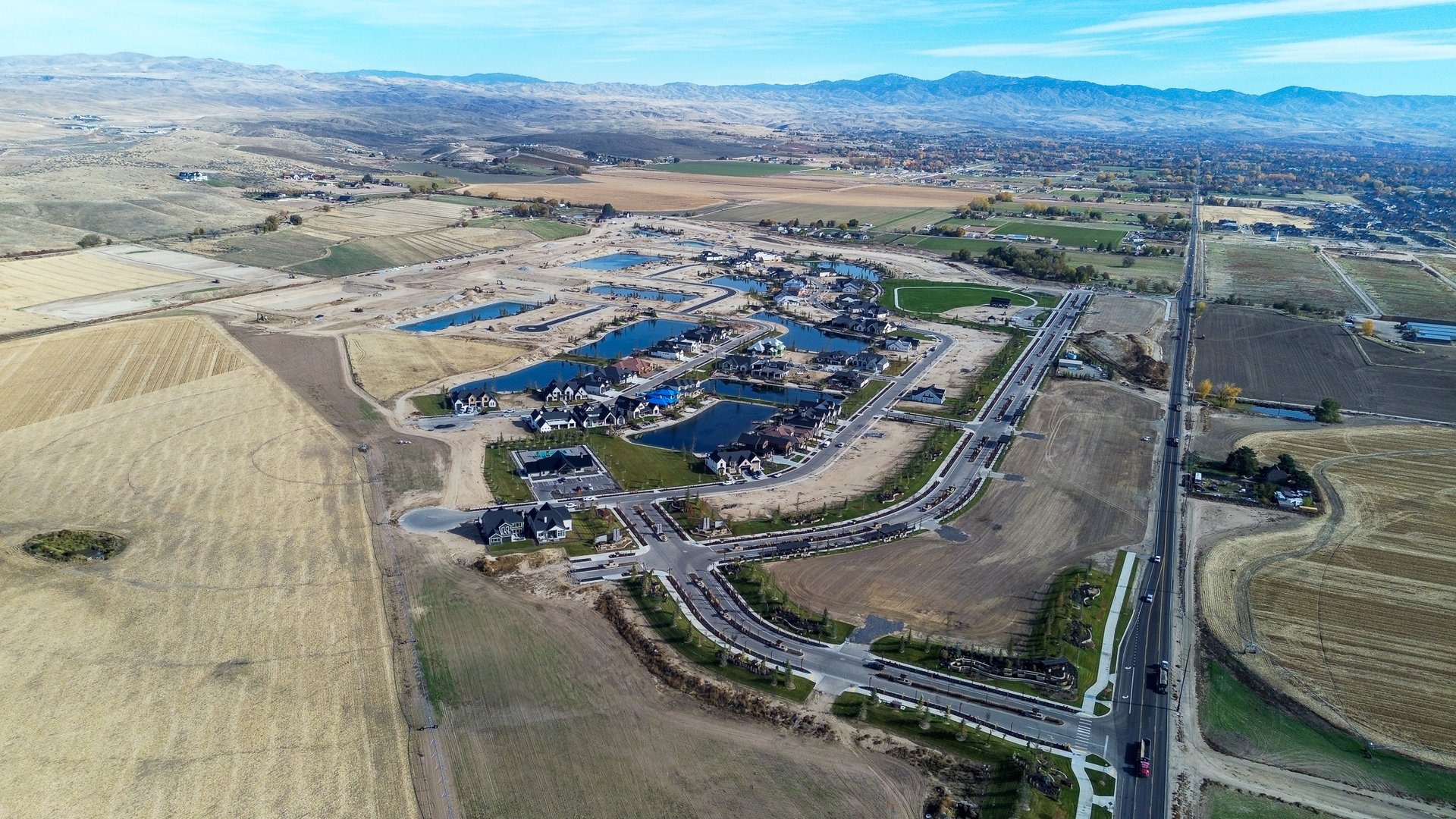 Aerial view of a housing development with ponds, unfinished lots, farmland, and distant mountains.