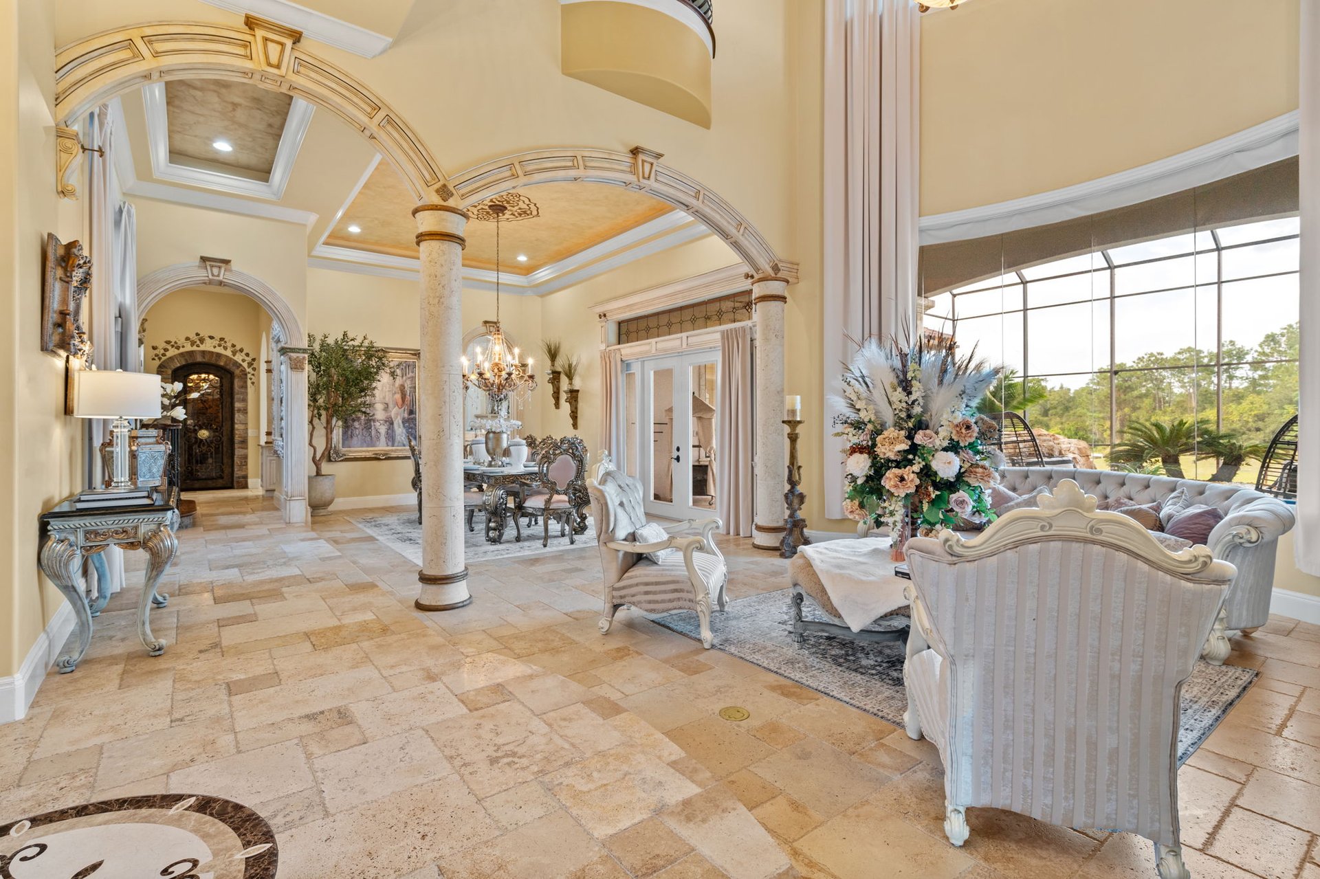 Furnished living and dining room with ornate arches, stone columns, and large windows.
