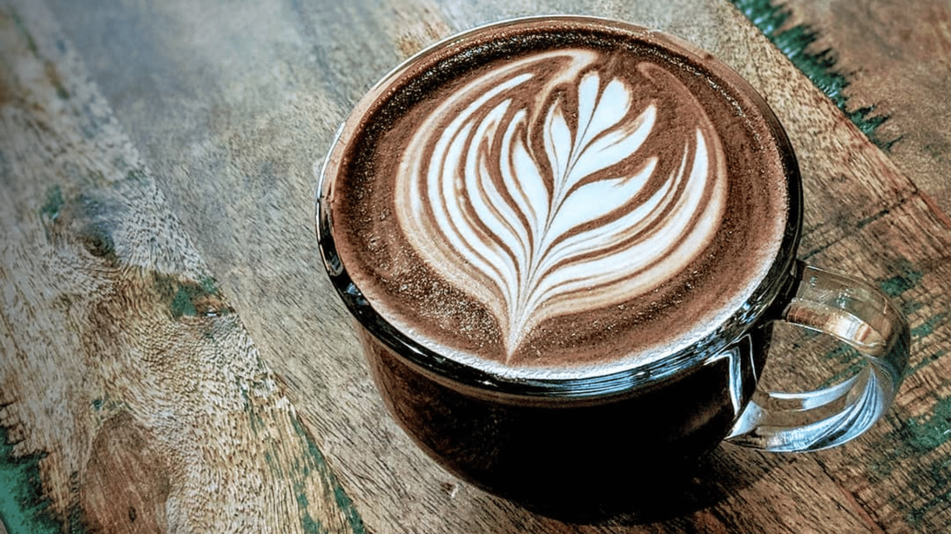 Beautiful rosetta latte art in glass cup on wooden table - Miami's skilled barista work featured by The Edit Real Estate