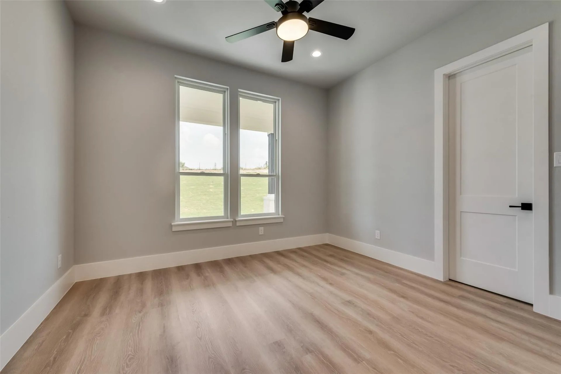 Vacant room with wood-look floors, two windows, and a ceiling fan with light.