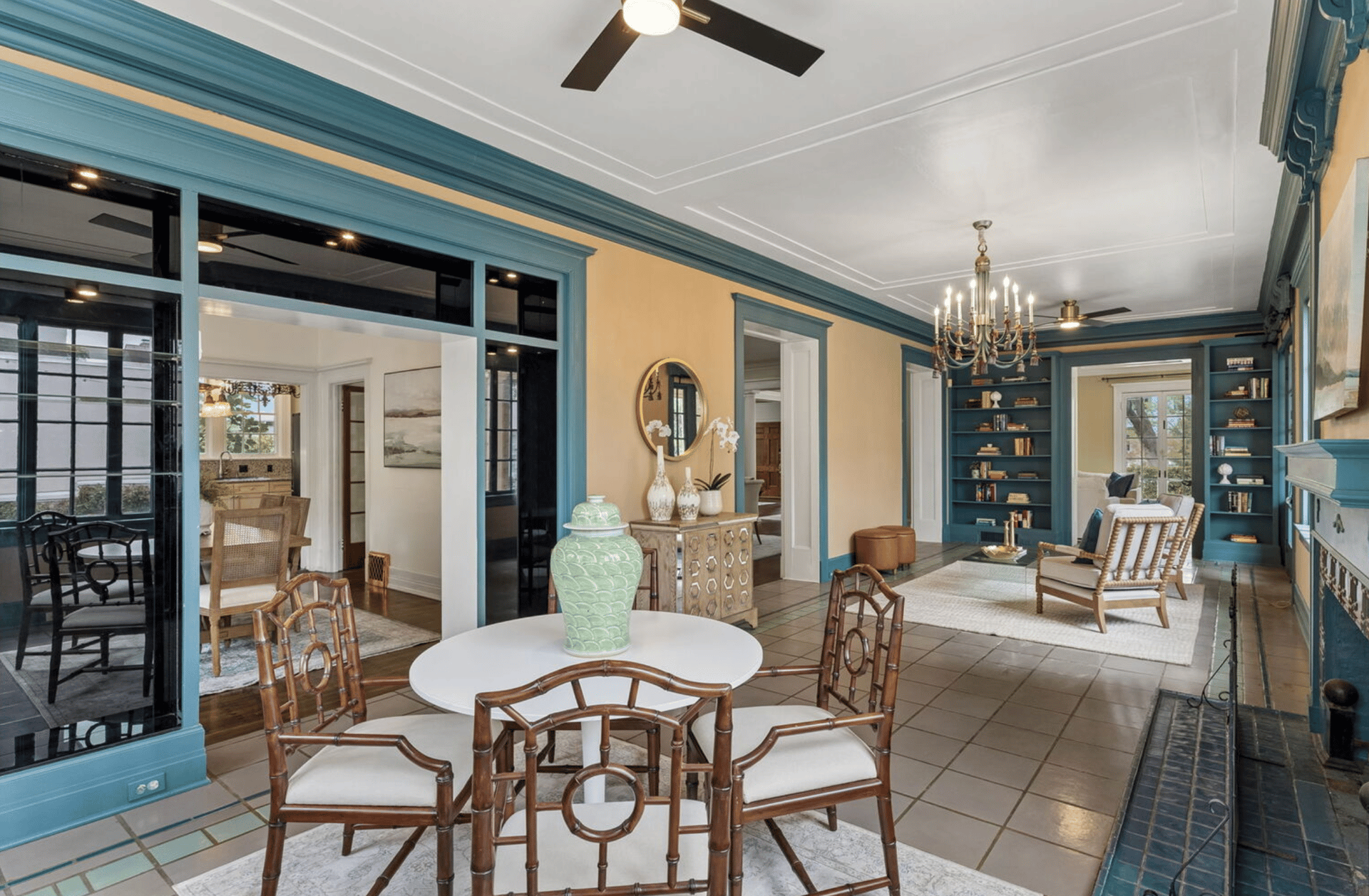 Living room with teal built-ins, a chandelier, tiled floor, and seating beside black-framed glass doors.