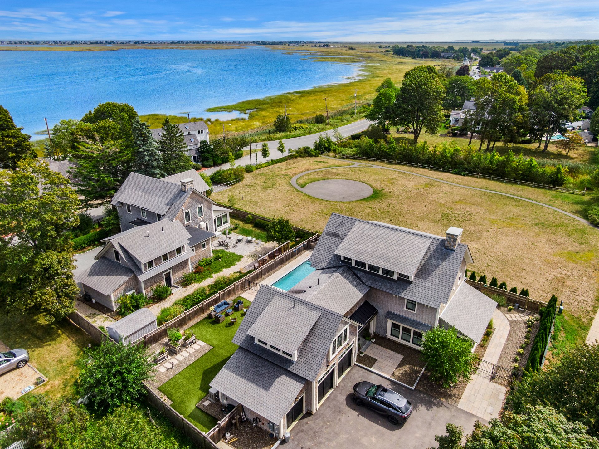 Aerial view of a gray-shingled home with a pool beside a coastal marsh and waterway.