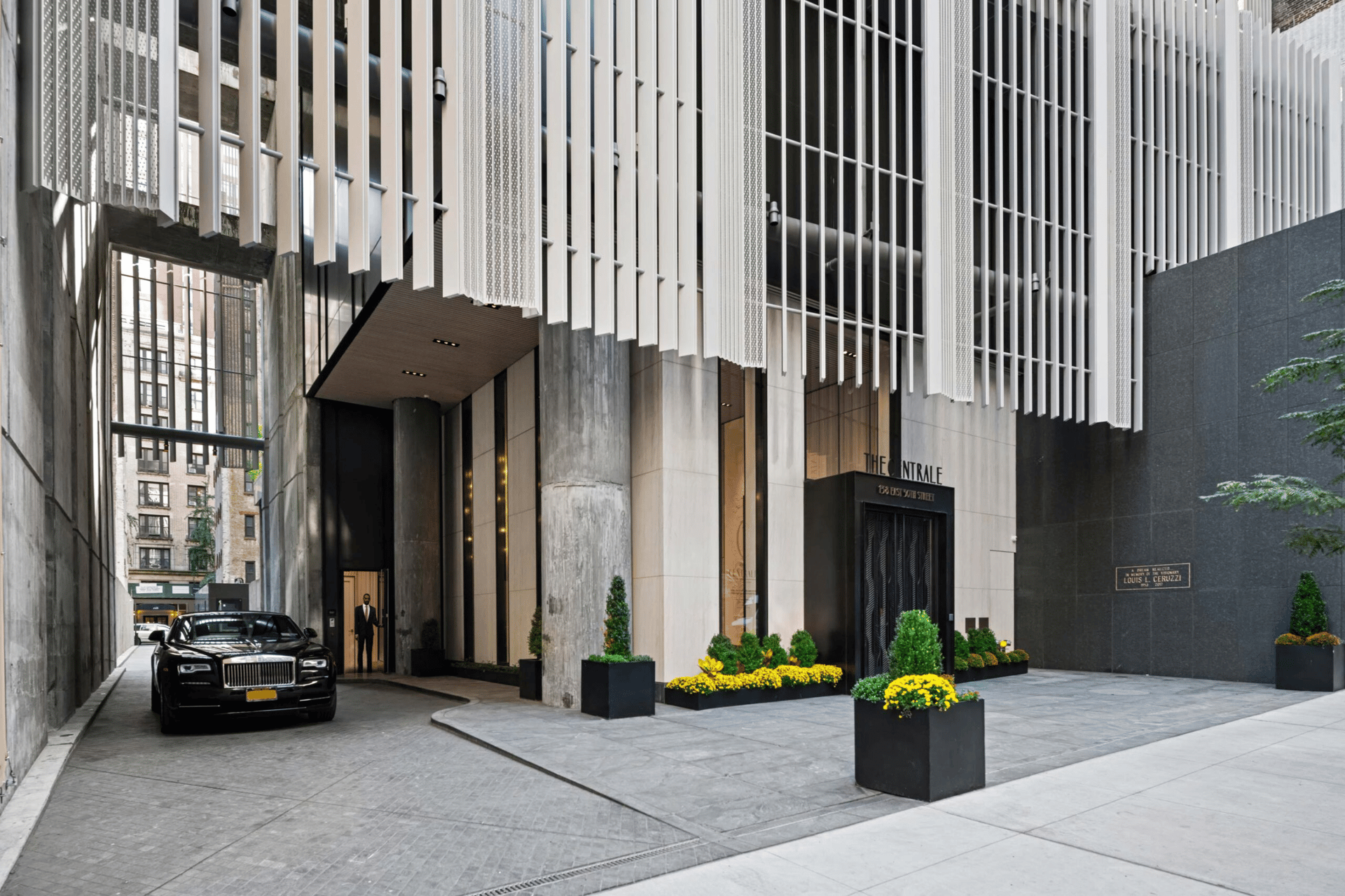 The Centrale entrance beneath tall white façade fins, with a black sedan and flower planters.
