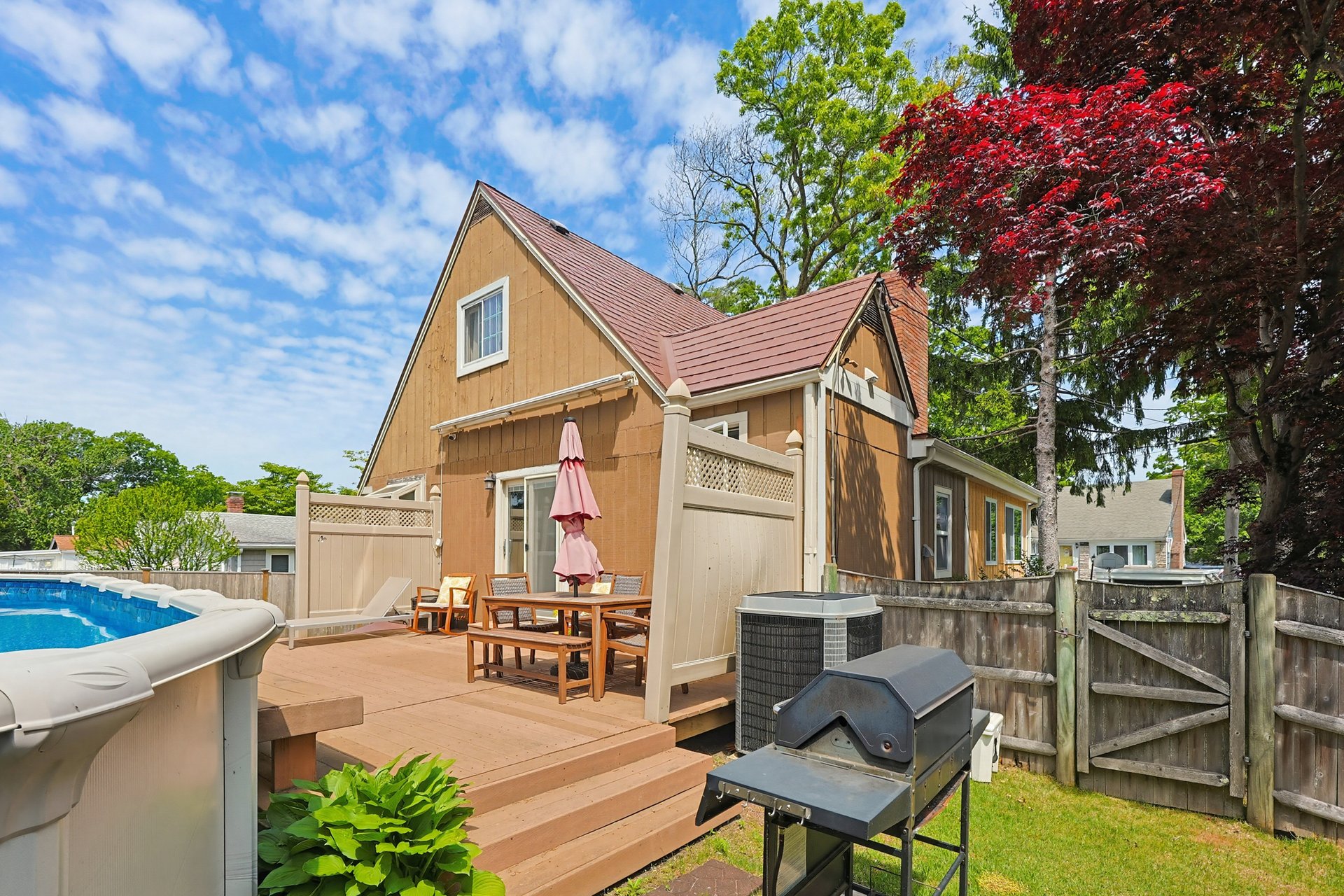 Backyard deck with patio dining set beside an above-ground pool and fenced yard.