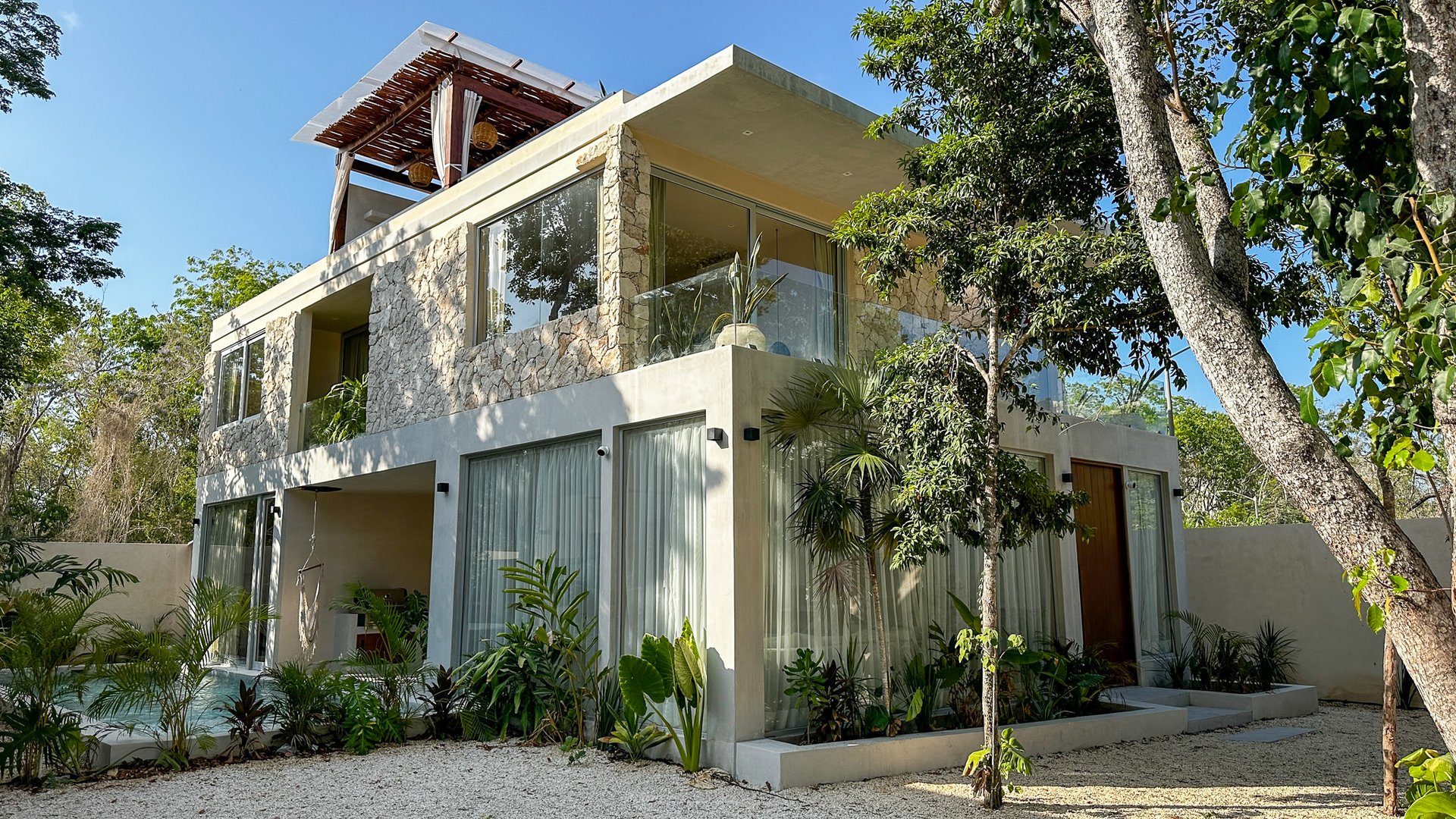 Modern stone-and-glass home with a rooftop pergola, tropical landscaping, and a small pool.