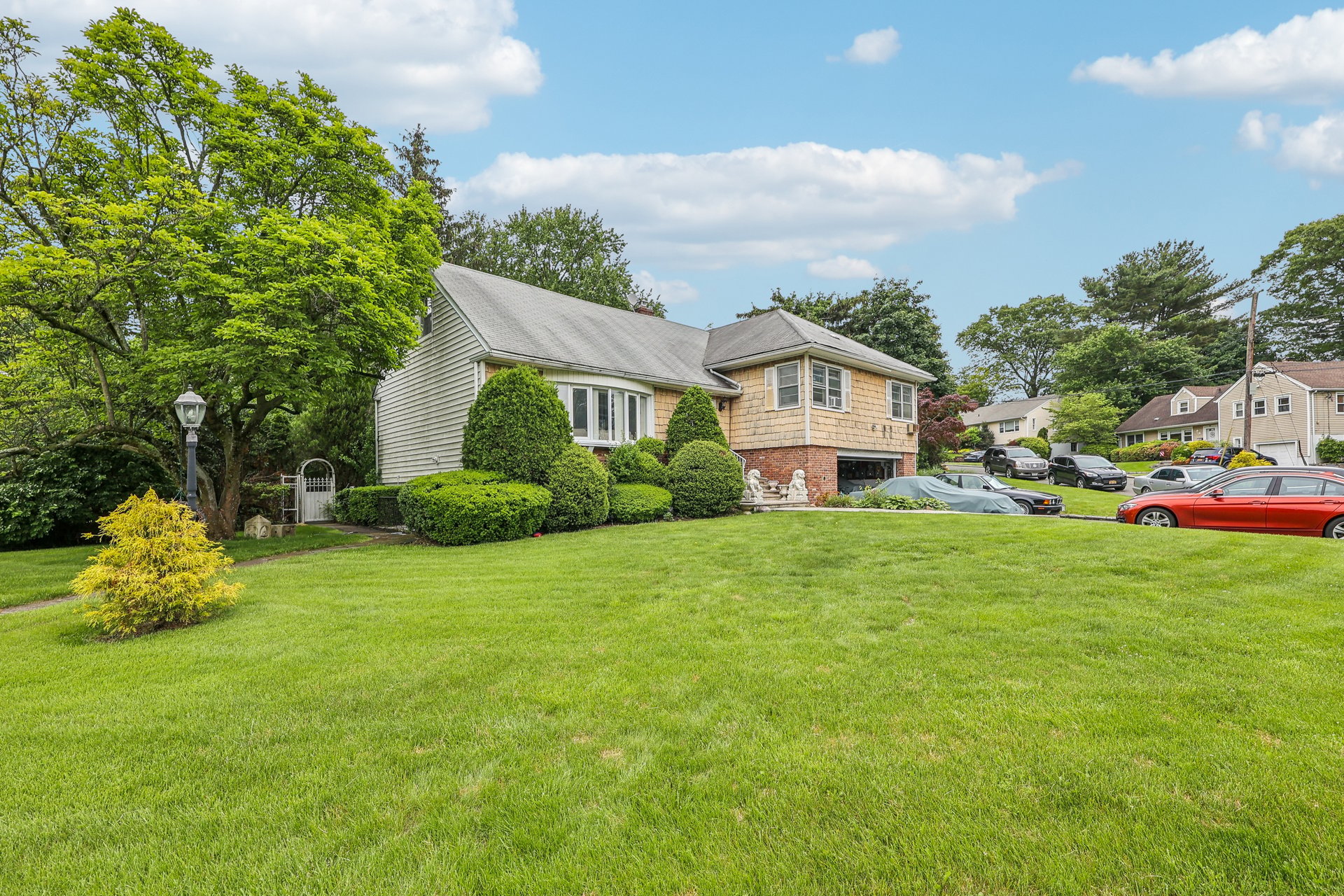 Split-level home with tan shingles, brick lower level, and a broad green lawn.