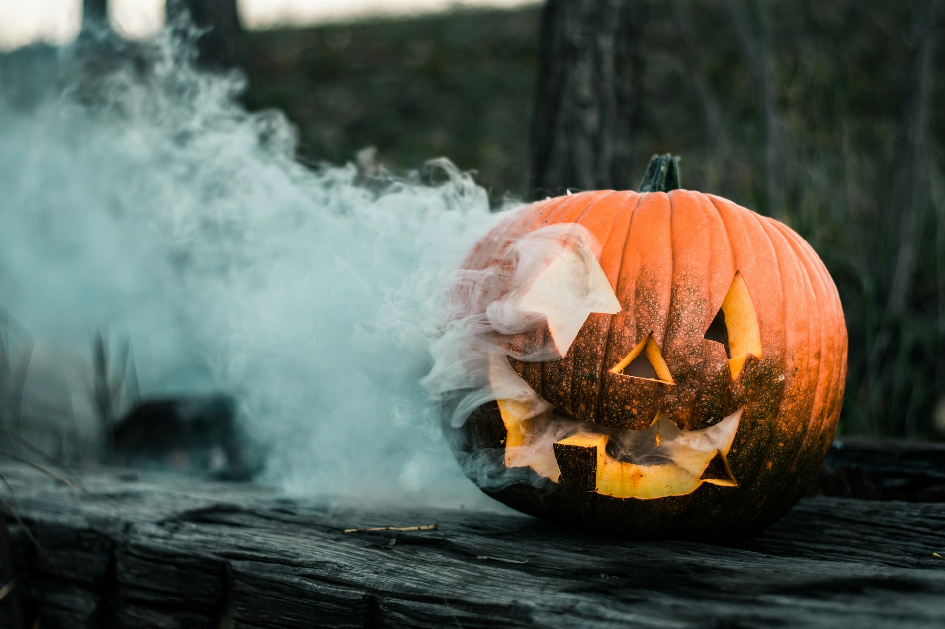 Smoking jack-o'-lantern with a carved smiling face on weathered boards.
