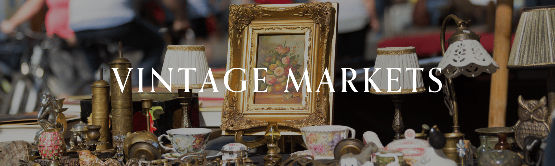 A collection of vintage items, including lamps, cups, and a framed painting, displayed at a market.