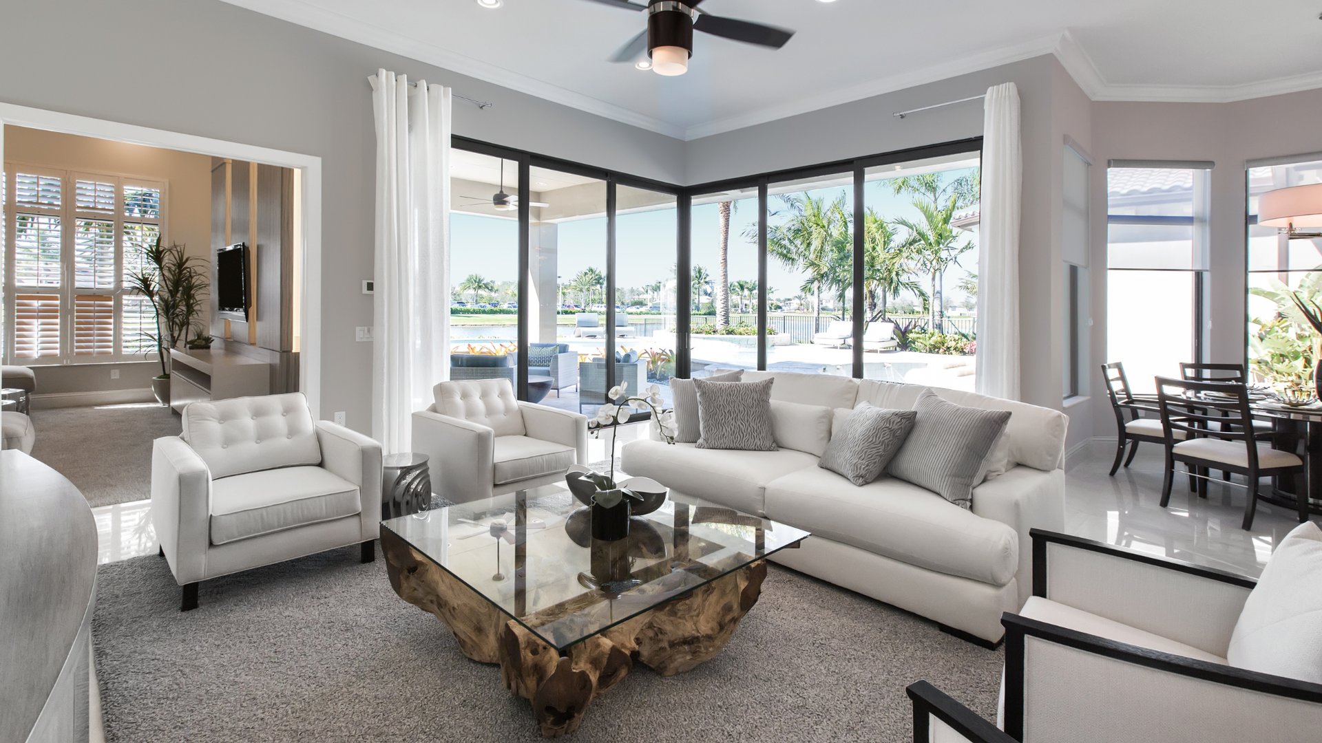 Bright modern living room with white furniture, glass coffee table, and floor-to-ceiling windows overlooking pool area, demonstrating professional home staging for Miami real estate listings by The Edit Real Estate