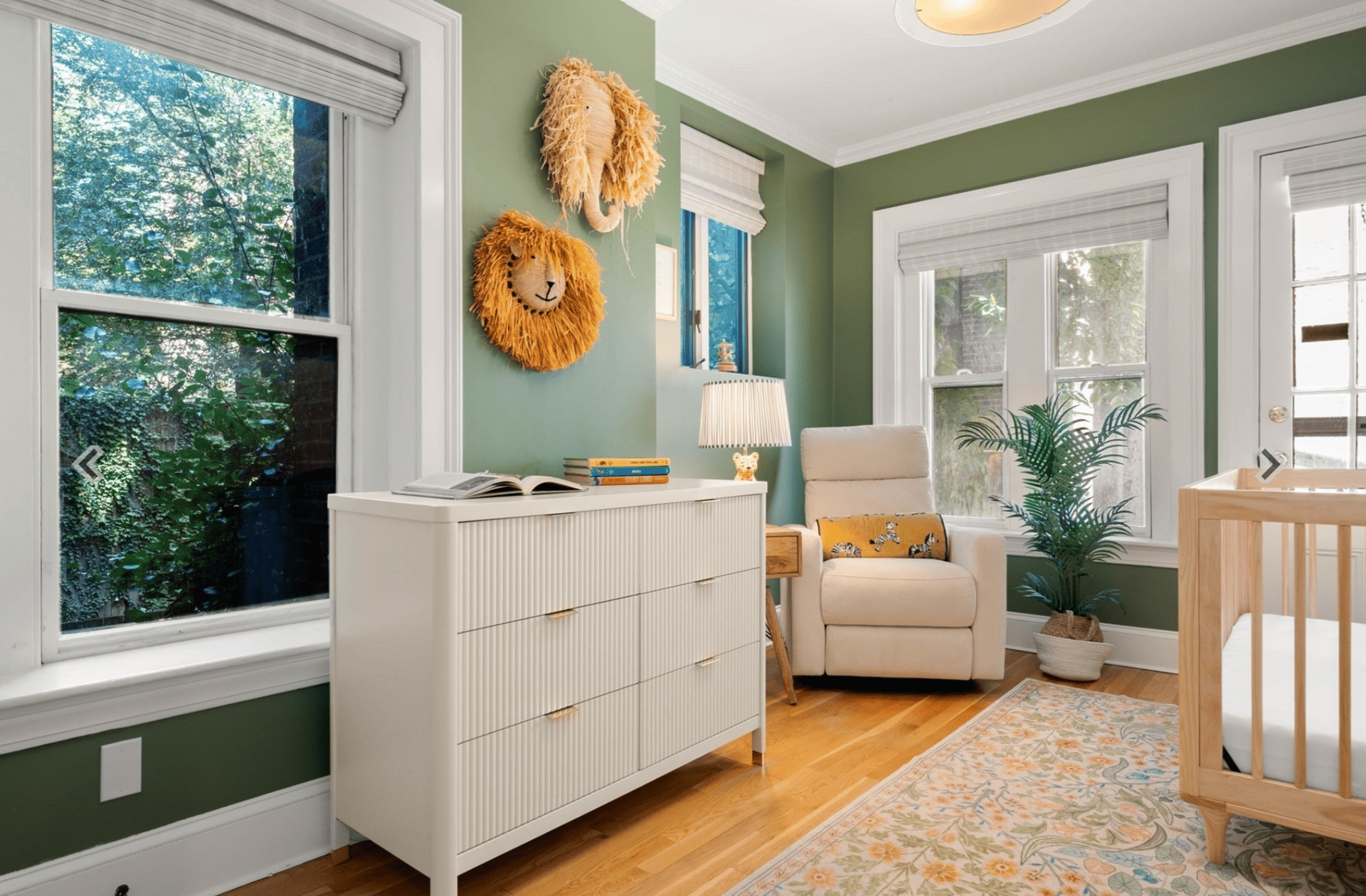 Nursery with a white crib, armchair, and lion wall decorations.