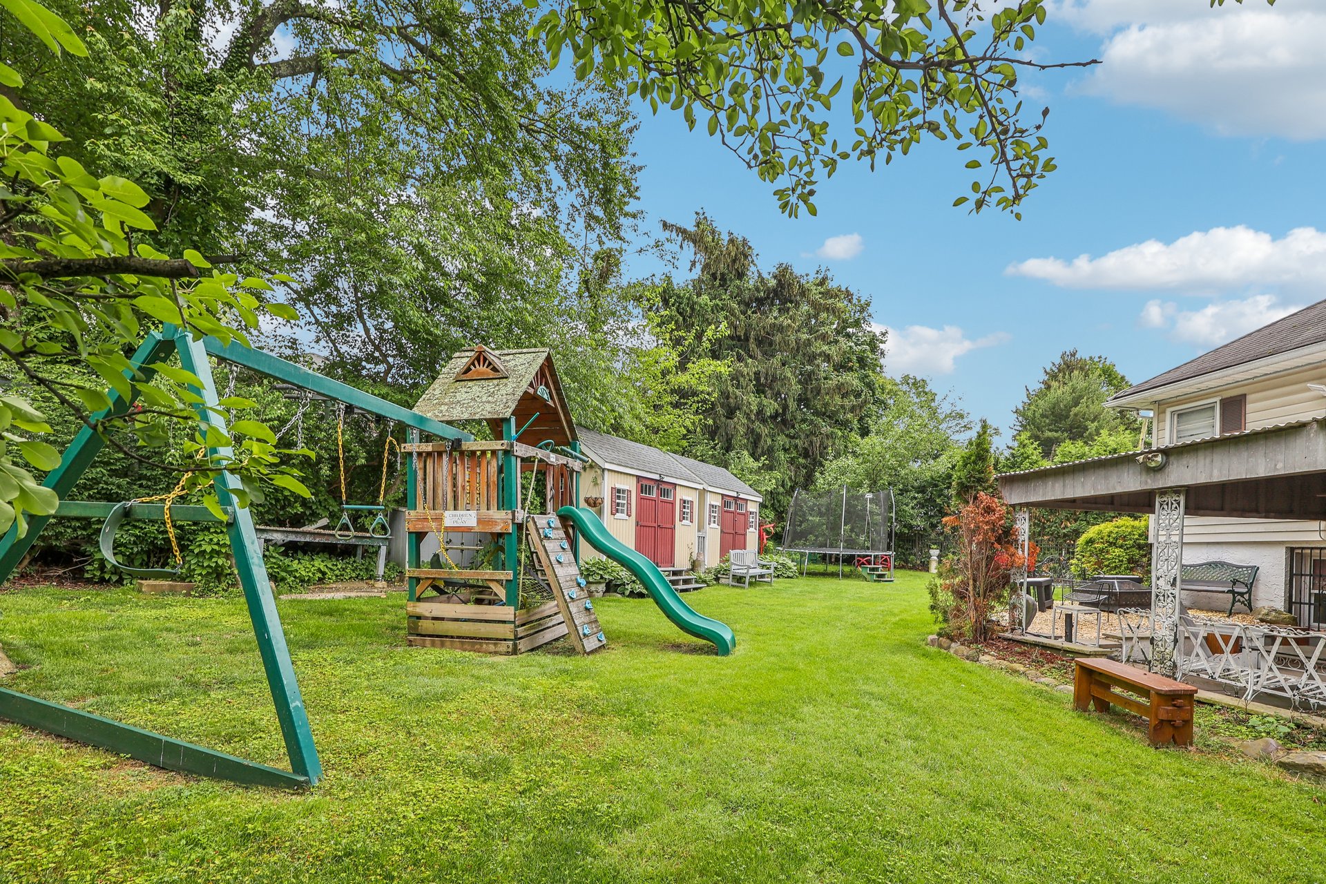 Backyard with a large wooden playset, shed, trampoline, and covered patio.