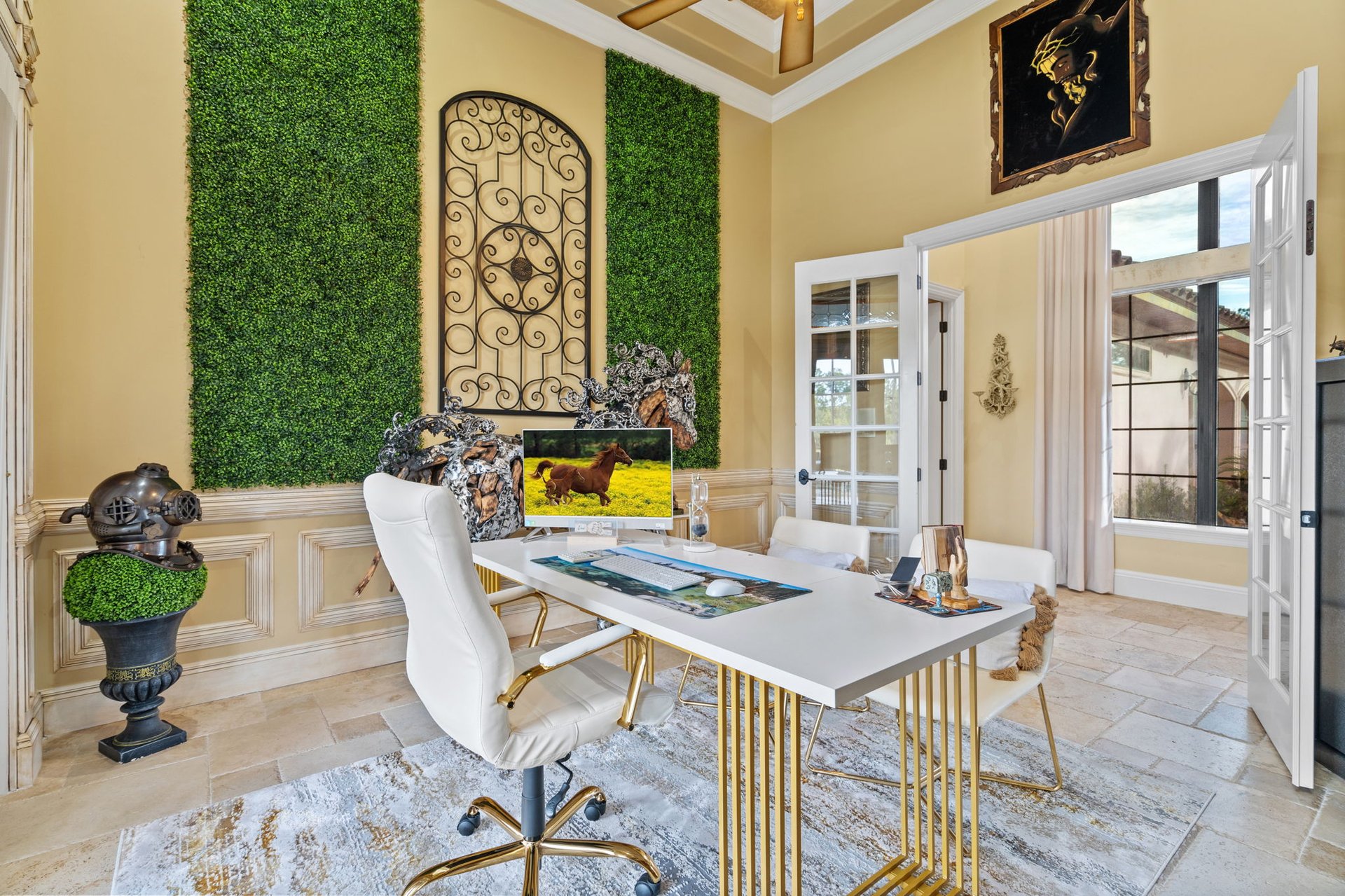 Home office with a white-and-gold desk, greenery wall panels, and open French doors.