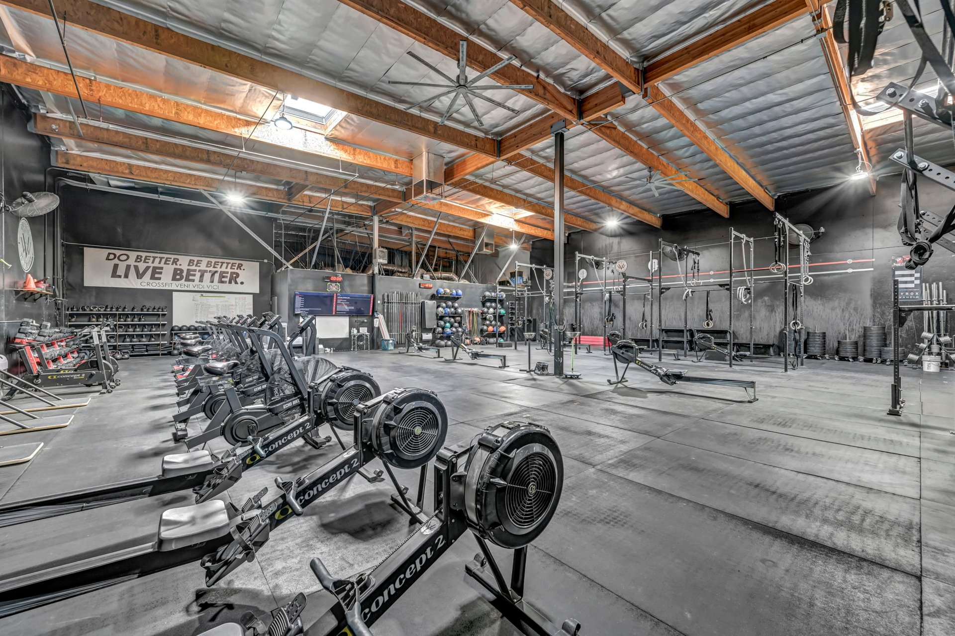 Gym interior with rowing machines, weightlifting racks, and exposed timber ceiling beams.