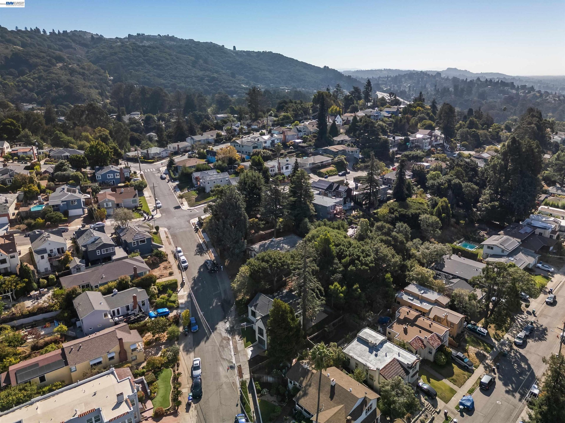 Aerial view of Oakland homes and tree-lined streets beneath wooded hills.