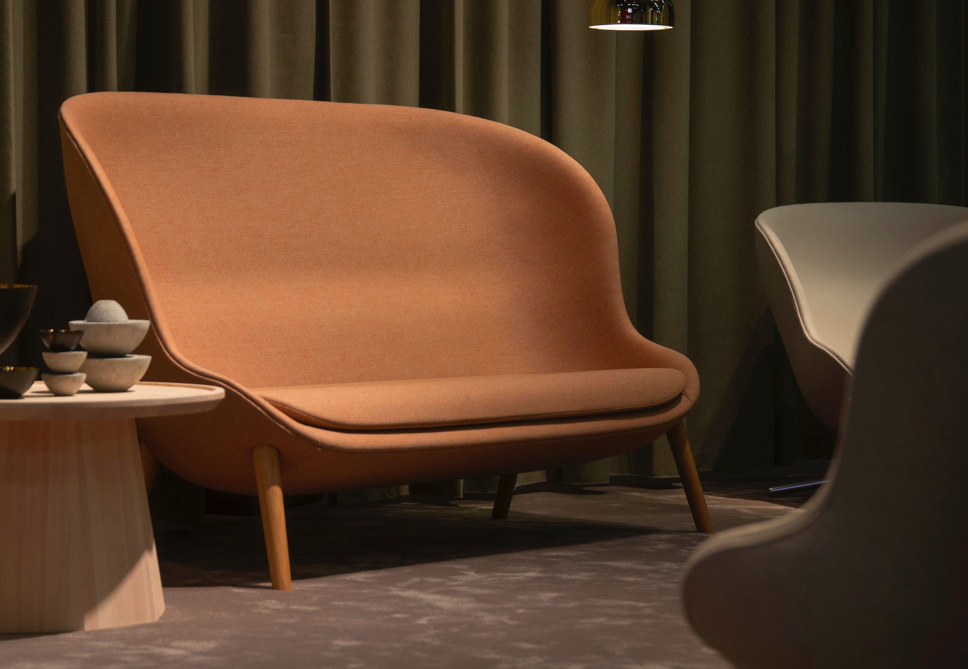 Rust-orange upholstered lounge chair with wooden legs beside a small table and ceramic bowls.
