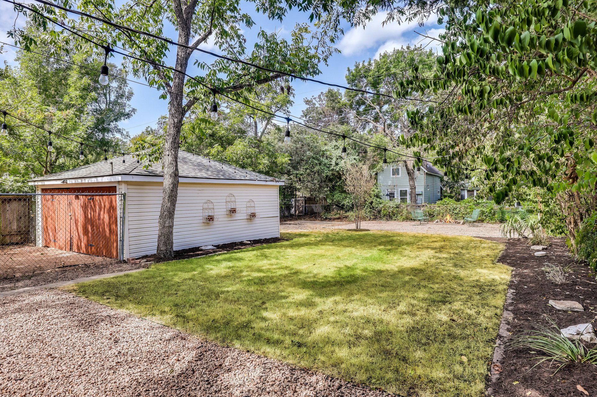 Backyard with a broad lawn, detached shed, overhead string lights, and gravel paving.