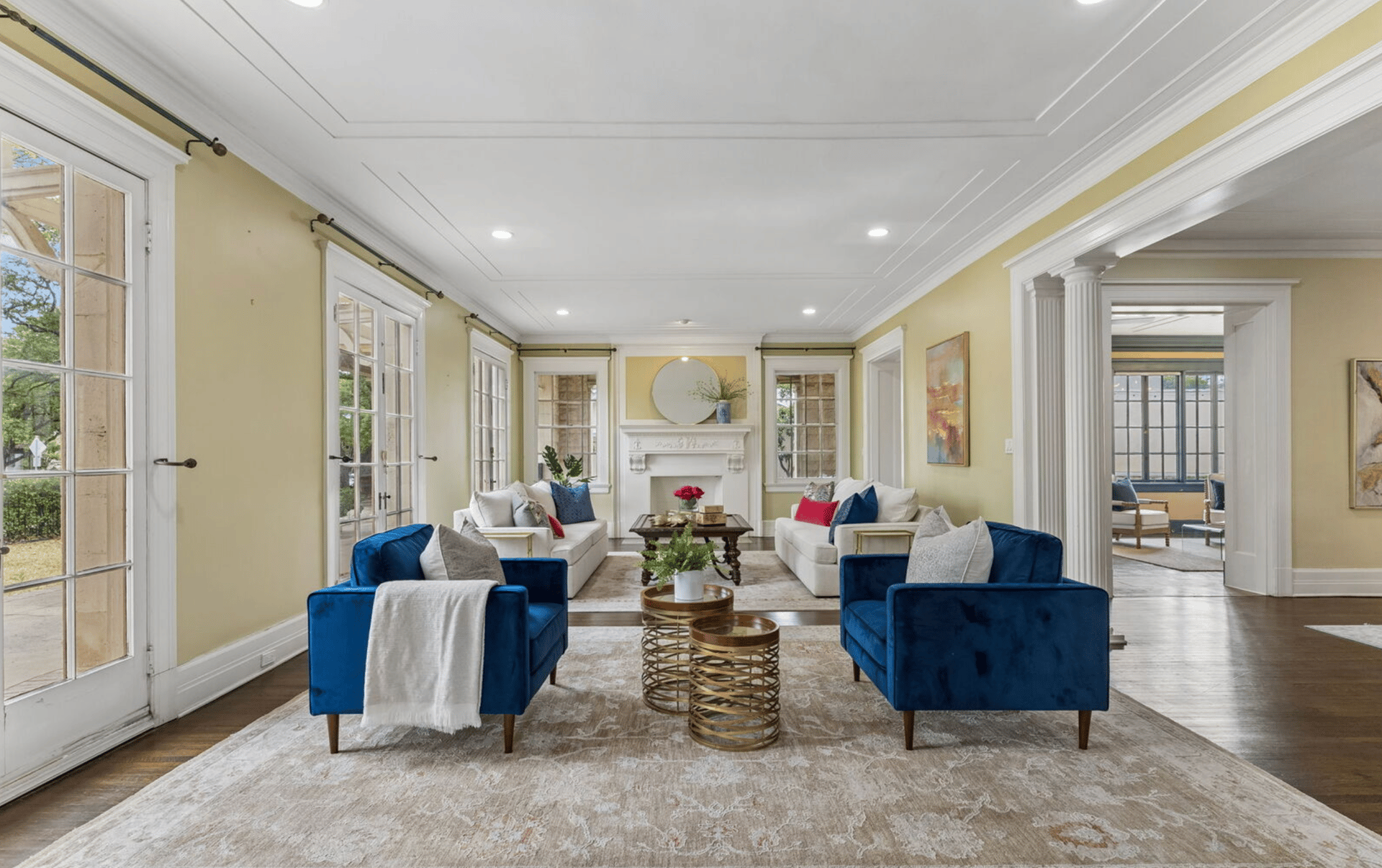 Staged living room with blue velvet armchairs, white sofas, and a decorative fireplace.