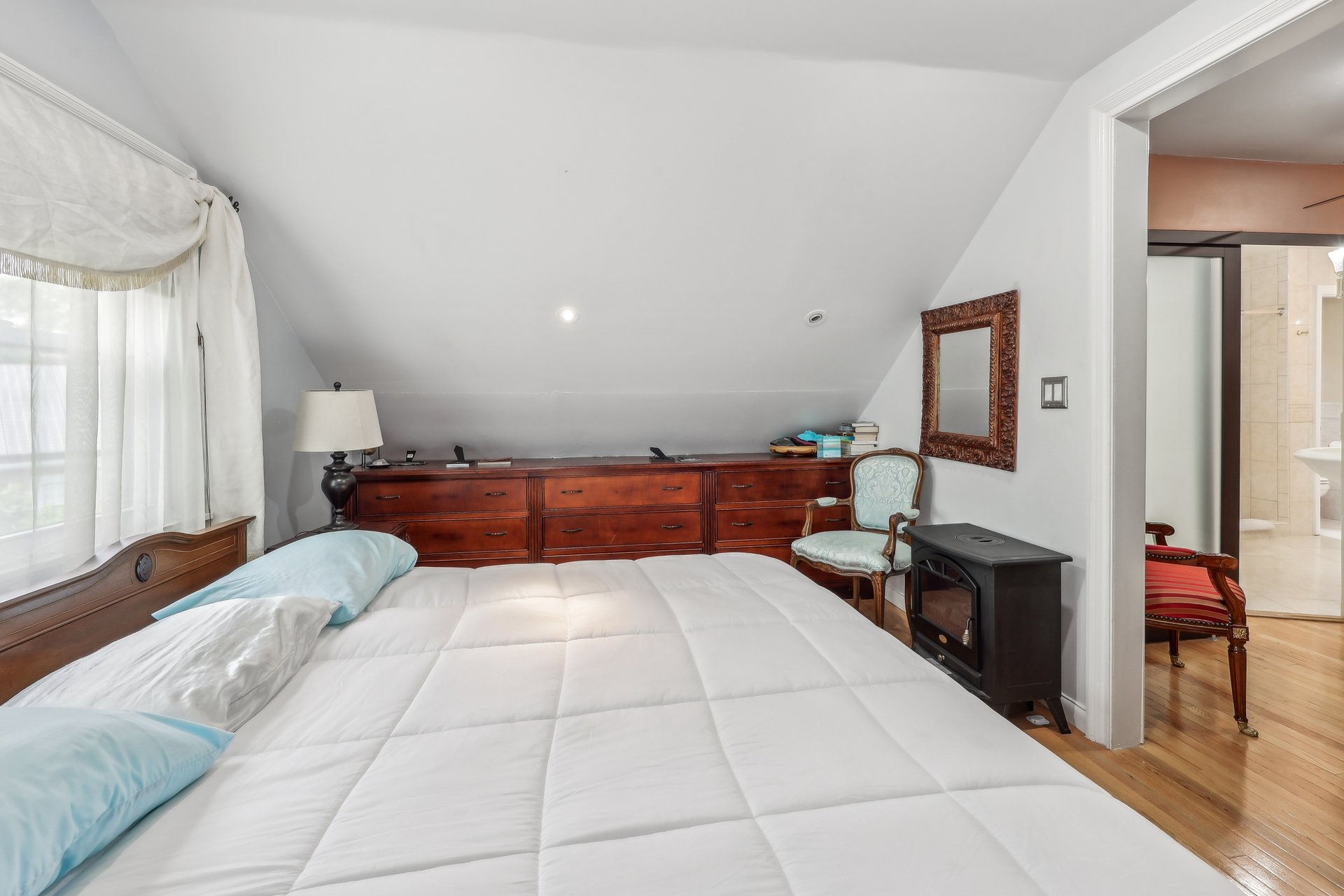 Attic bedroom with a white bed, sloped ceiling, and long dark wood dresser.