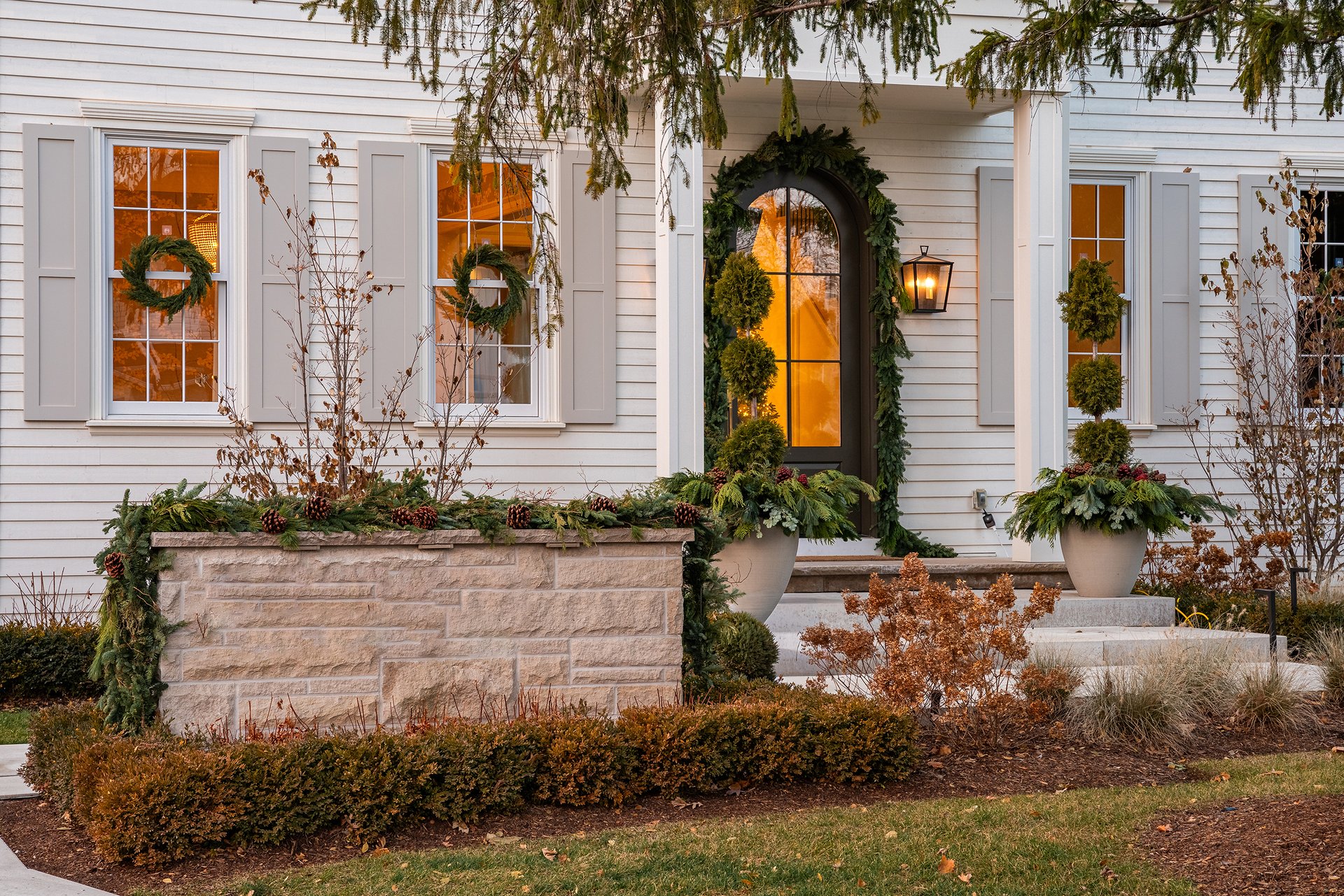 Front entry of an Oakville custom home with arched door, fresh greenery garland, holiday planters, and traditional wreaths.