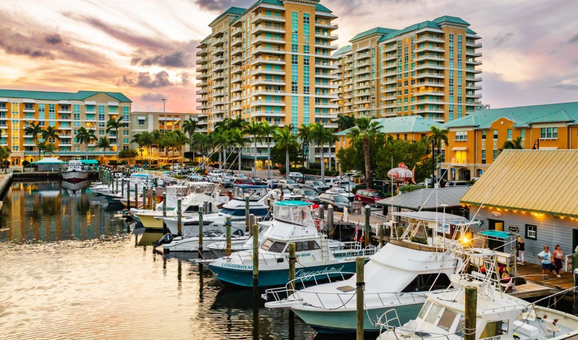 Waterfront condominium buildings and a marina crowded with boats at sunset.
