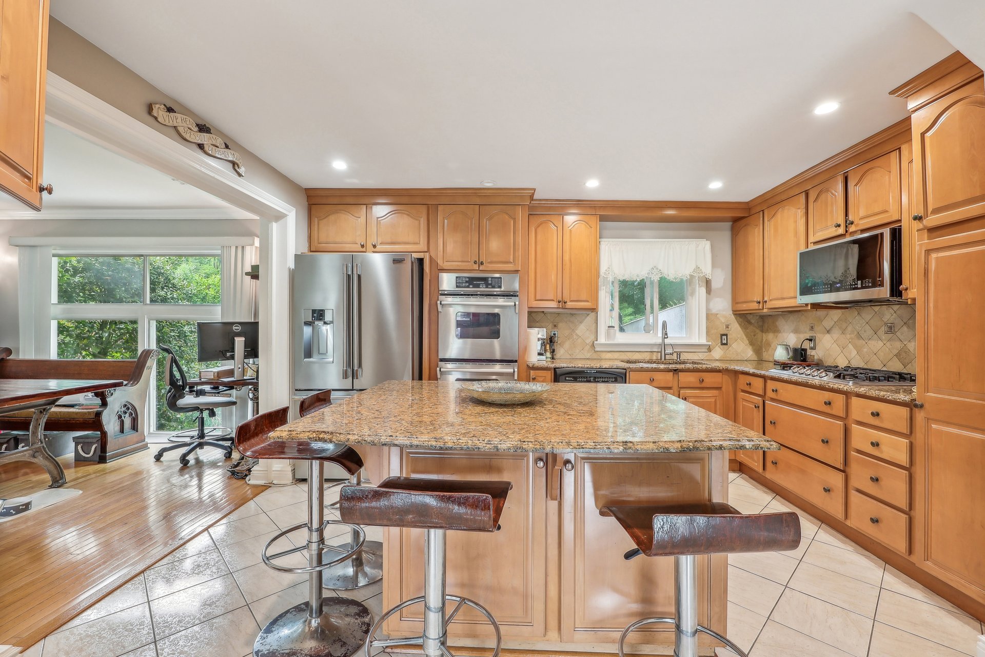 Kitchen with honey-colored cabinets, stainless appliances, and a large granite island with bar stools.