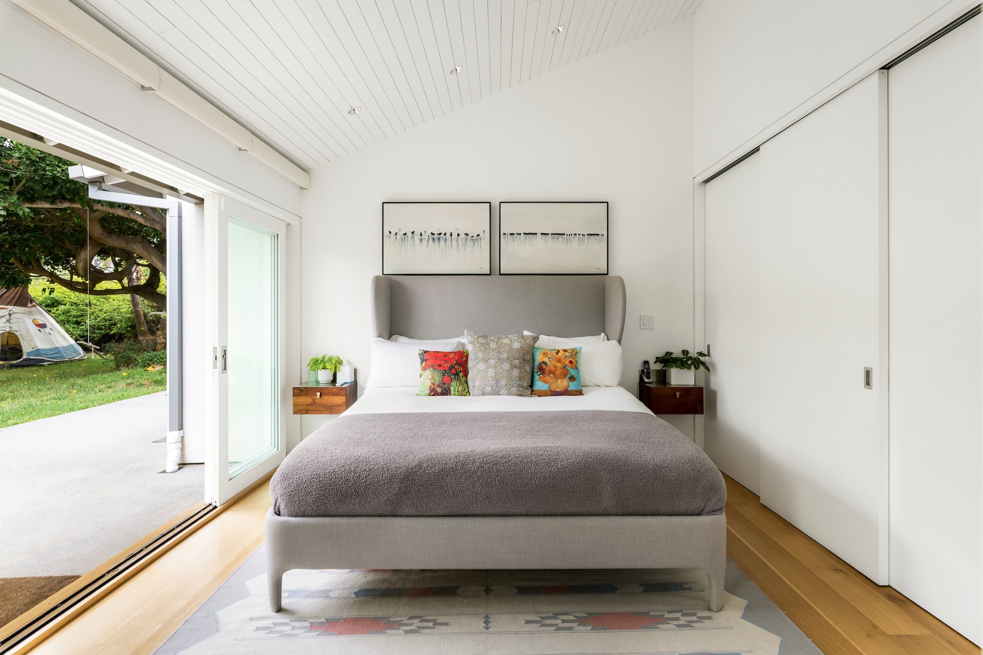 Bedroom with a gray upholstered bed and sliding doors opening onto a garden.