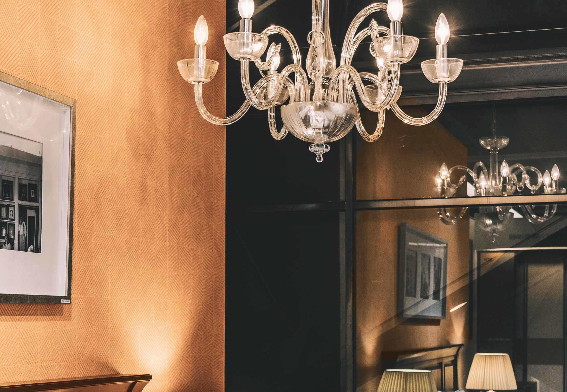 Glass chandelier reflected in a large mirror against patterned peach wallpaper.