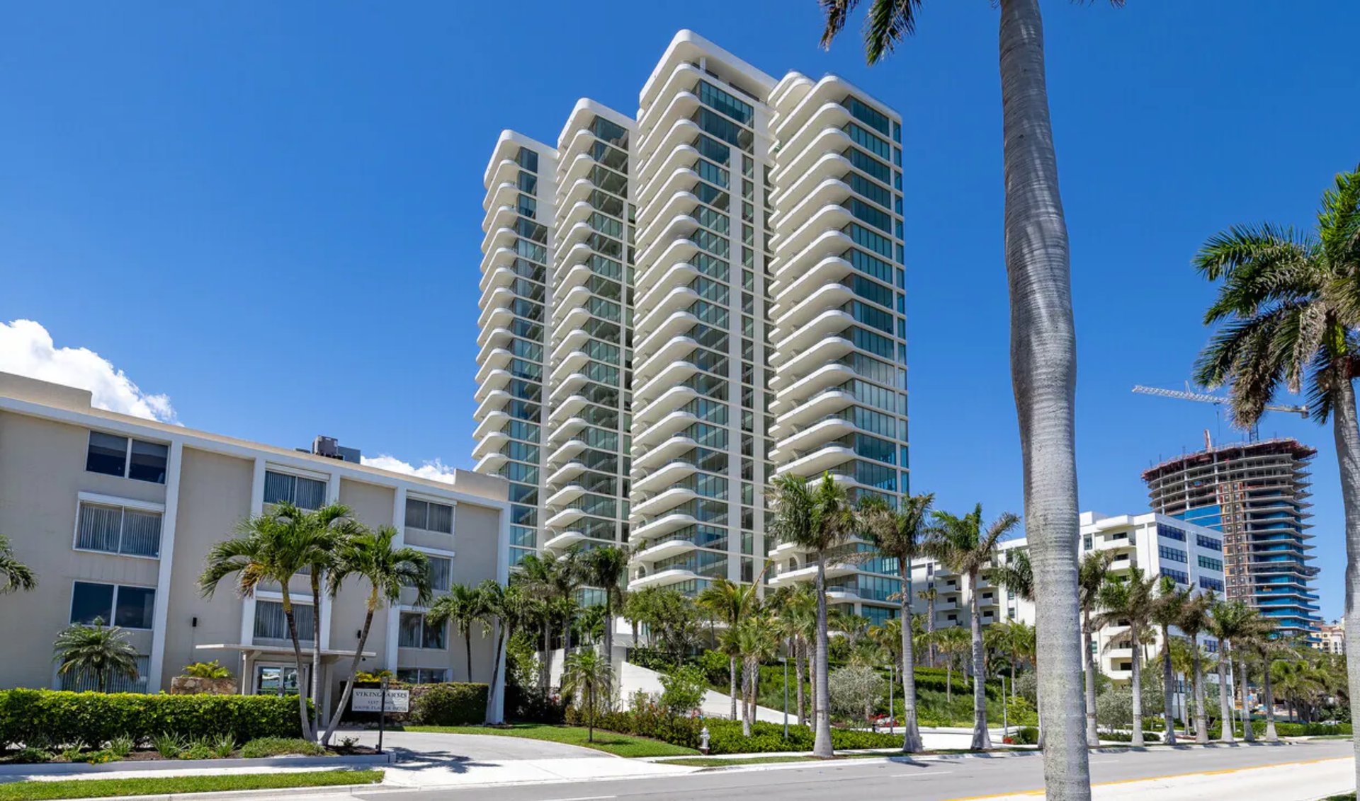 Luxury condominium towers with curved white balconies and palm trees along a sunny street.