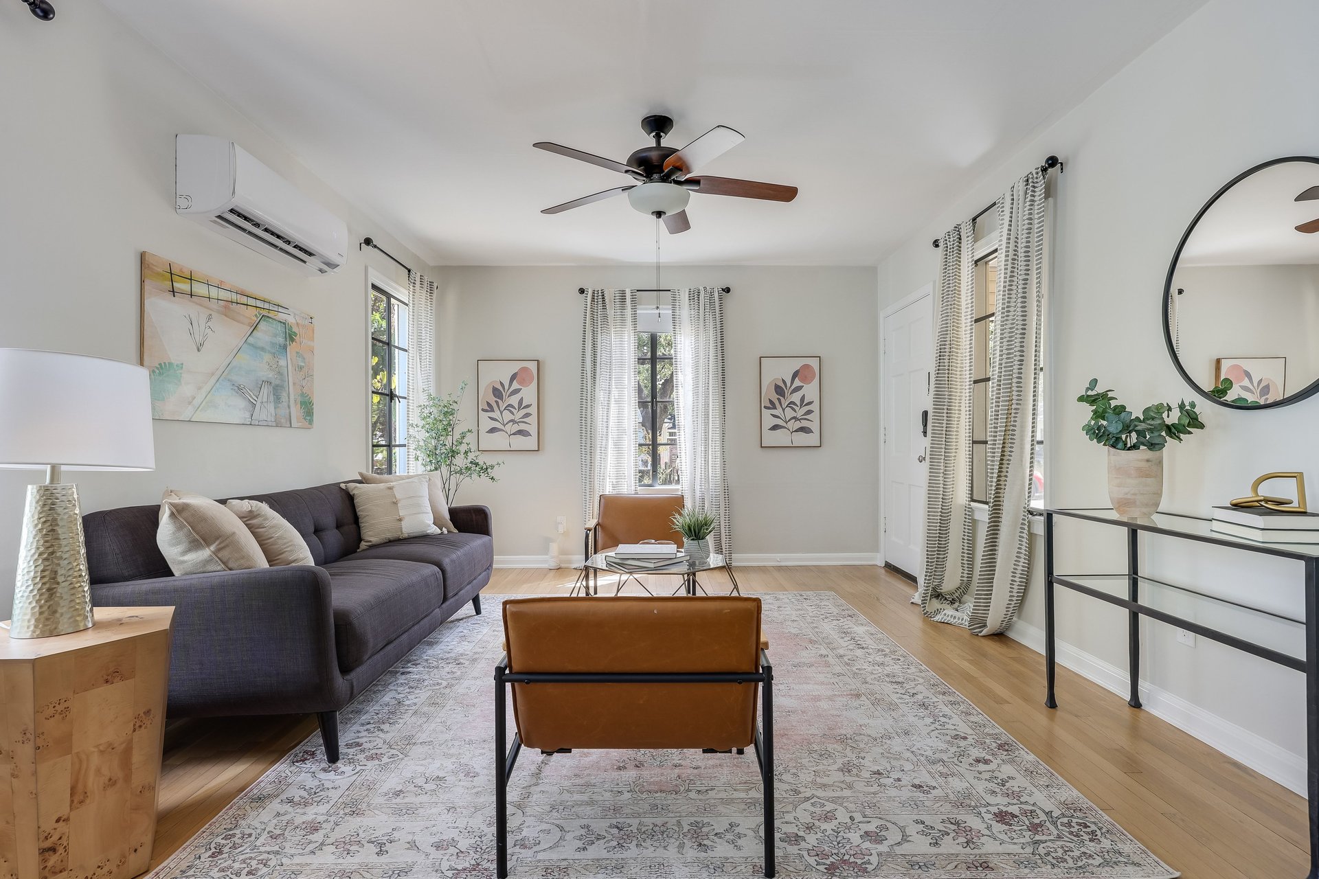 Living room with a dark sofa, leather chairs, patterned rug, and bright curtained windows.