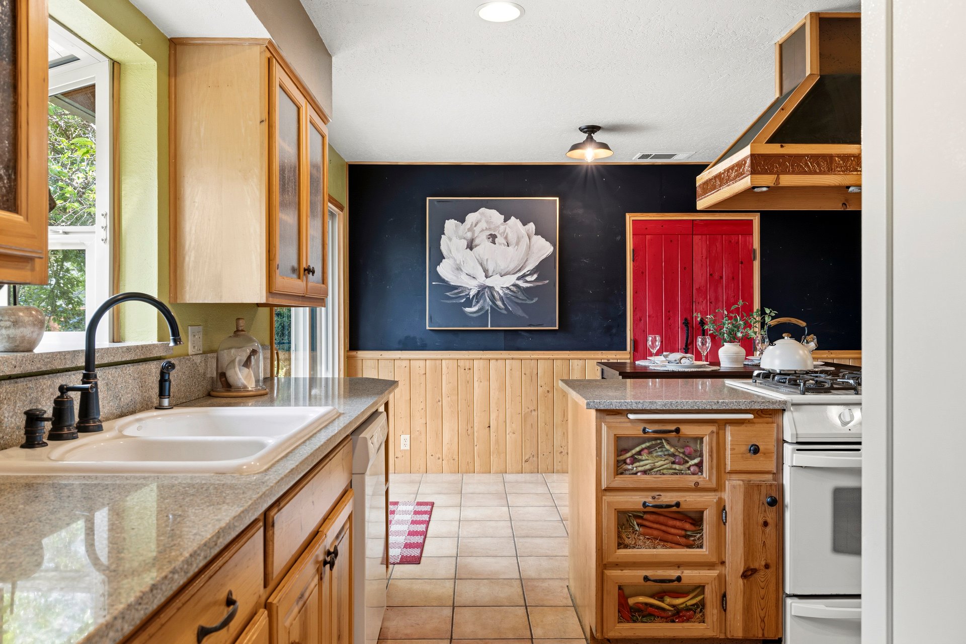 Kitchen with natural wood cabinets, a central island with produce bins, and a navy wall with flower artwork.