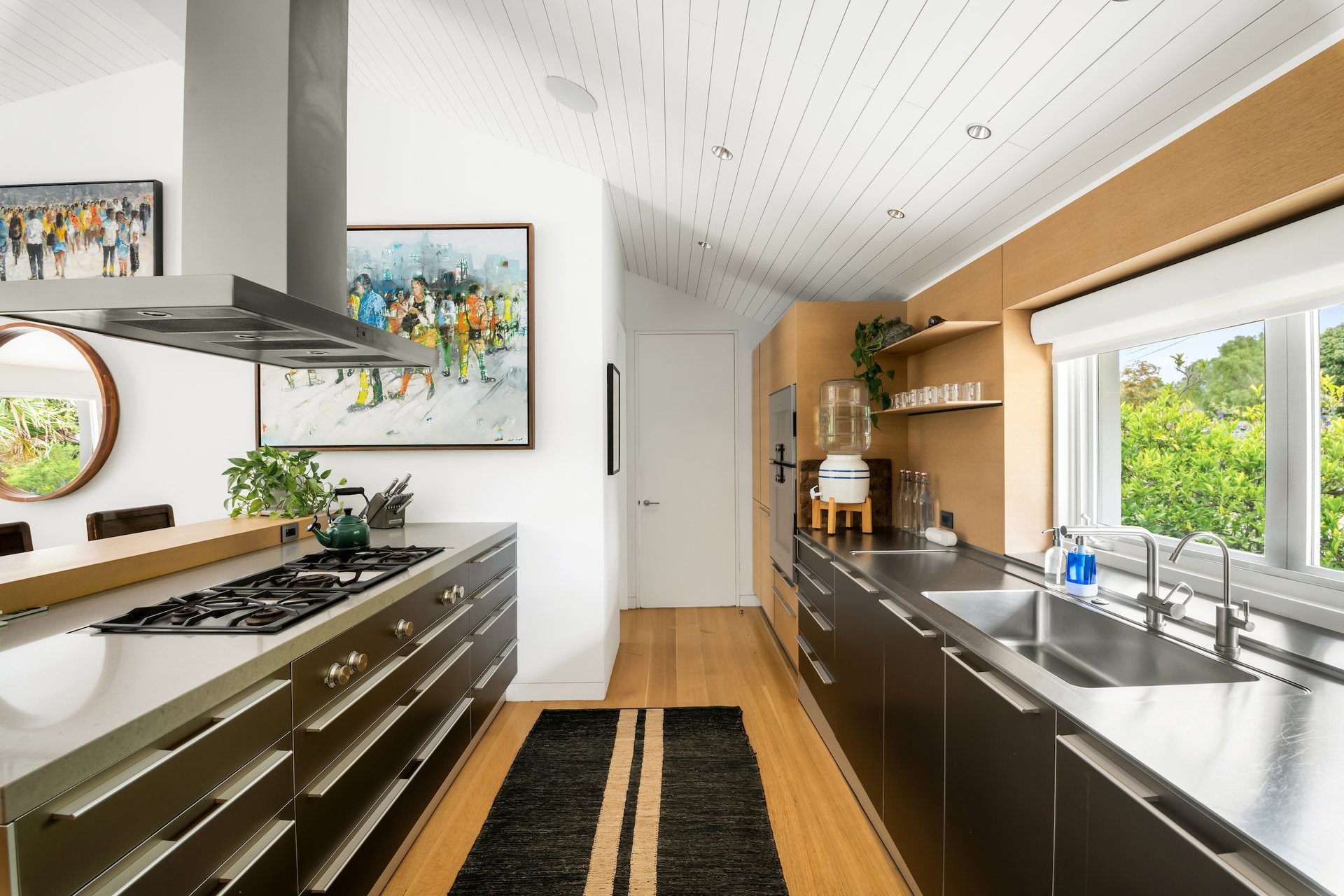 Modern kitchen with dark cabinetry, a long island cooktop, and a sink overlooking greenery.