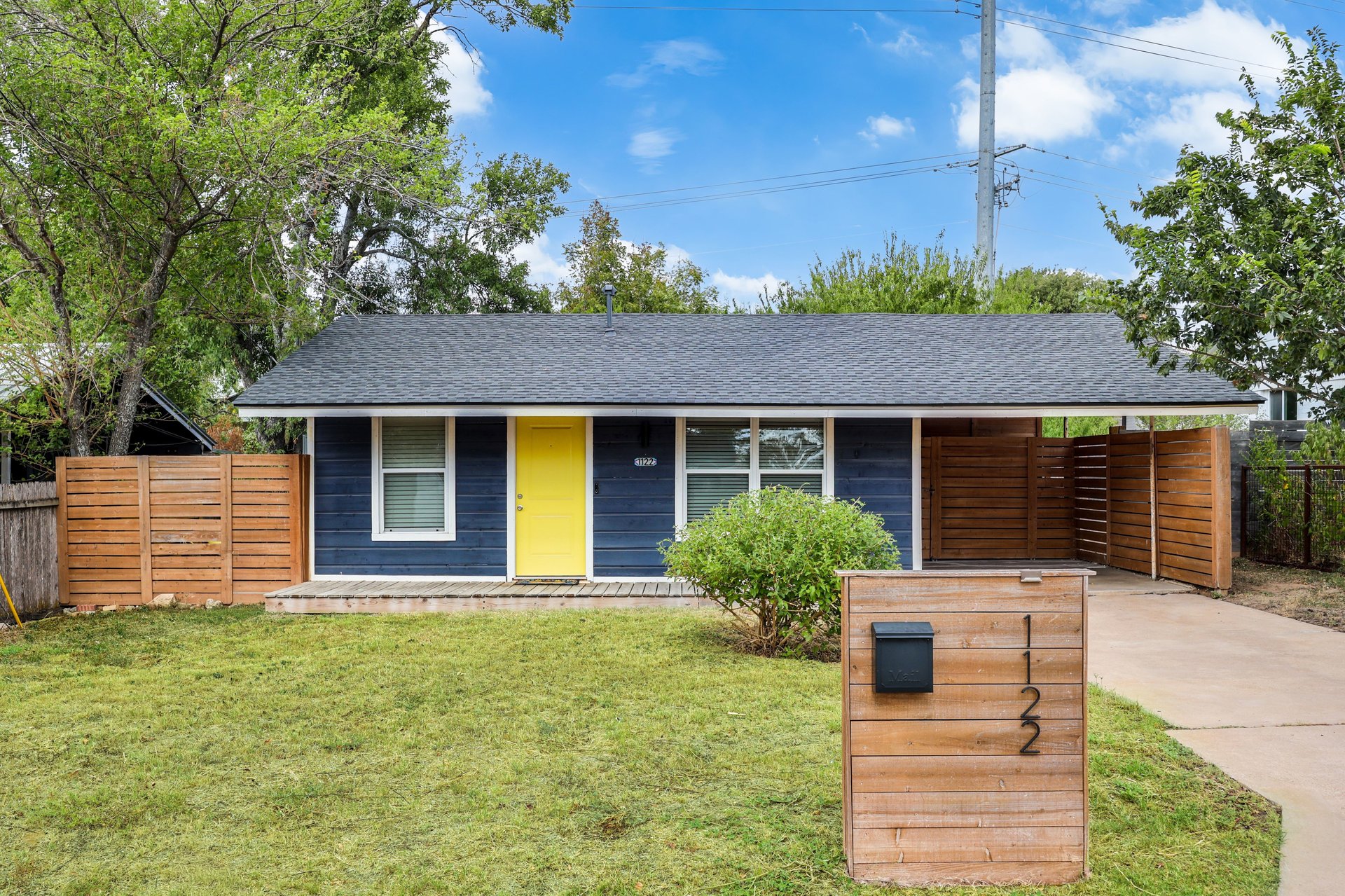 Blue single-story house with a yellow front door, wood privacy fences, and a front lawn.